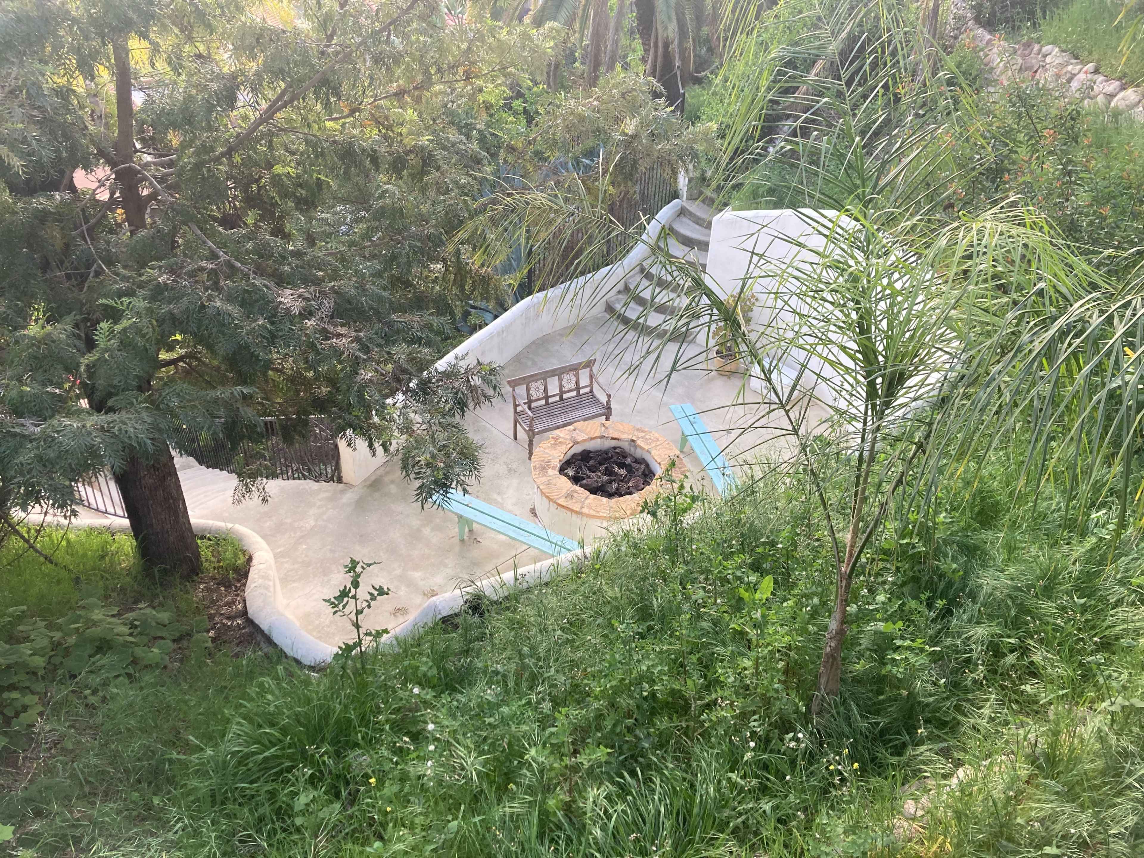 A circular fire pit surrounded by a concrete area, with a bench positioned nearby, set within a lush green landscape.