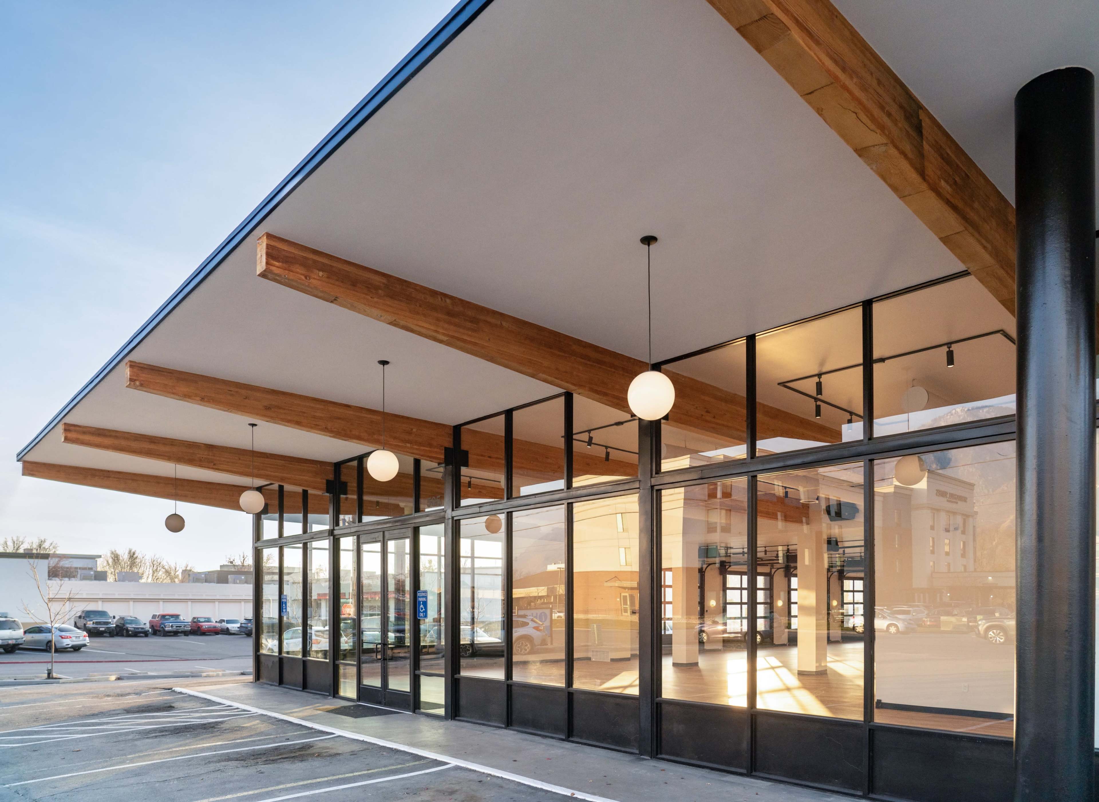 The image shows a modern storefront with large glass windows and wooden beams on the ceiling, located in a parking area.
