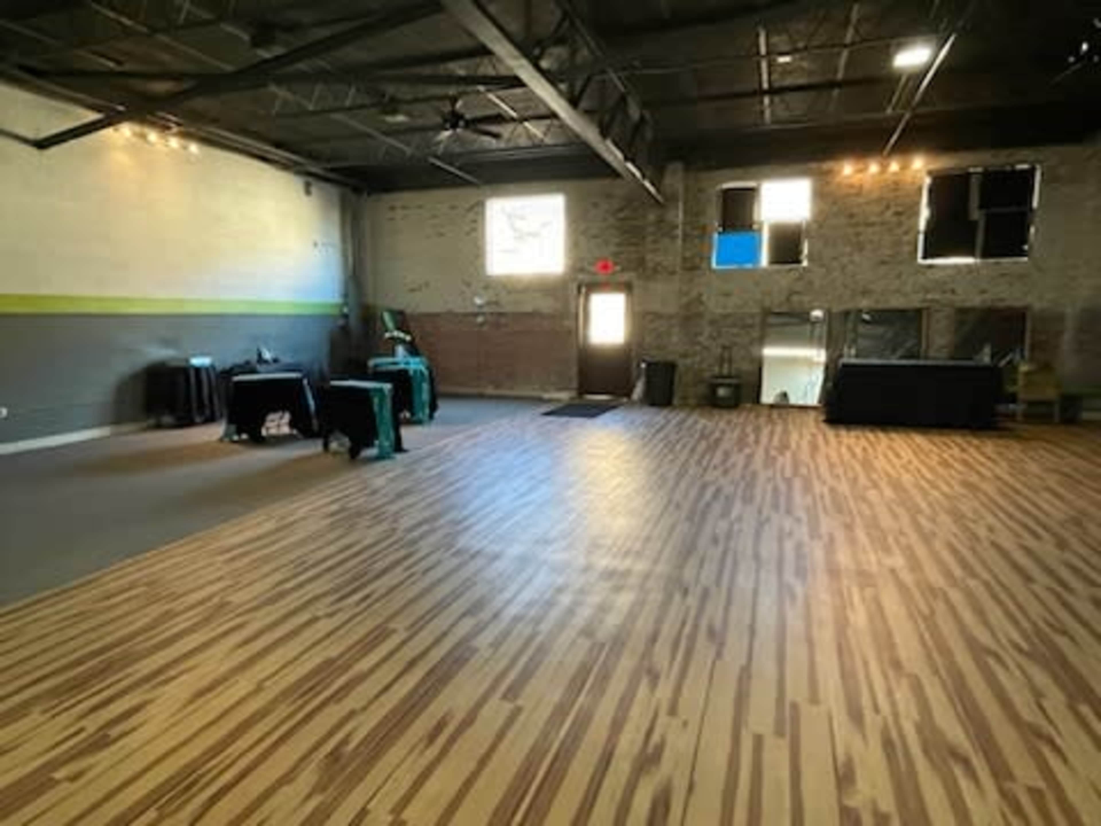 A spacious room with wooden floors, tables covered in black cloth, and a door leading outside.