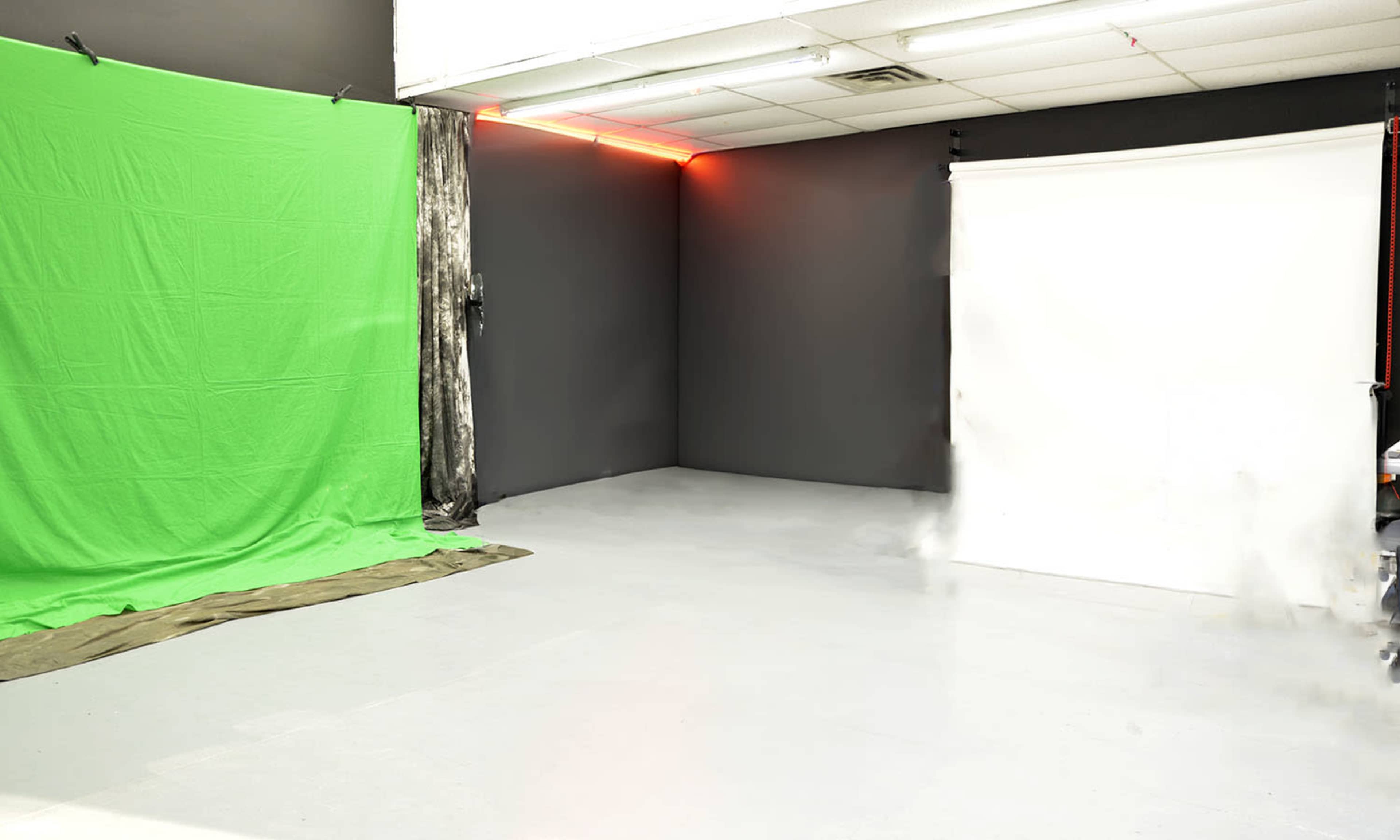 A studio setup featuring a green screen on the left, a white backdrop on the right, and a fog machine producing mist near the center.