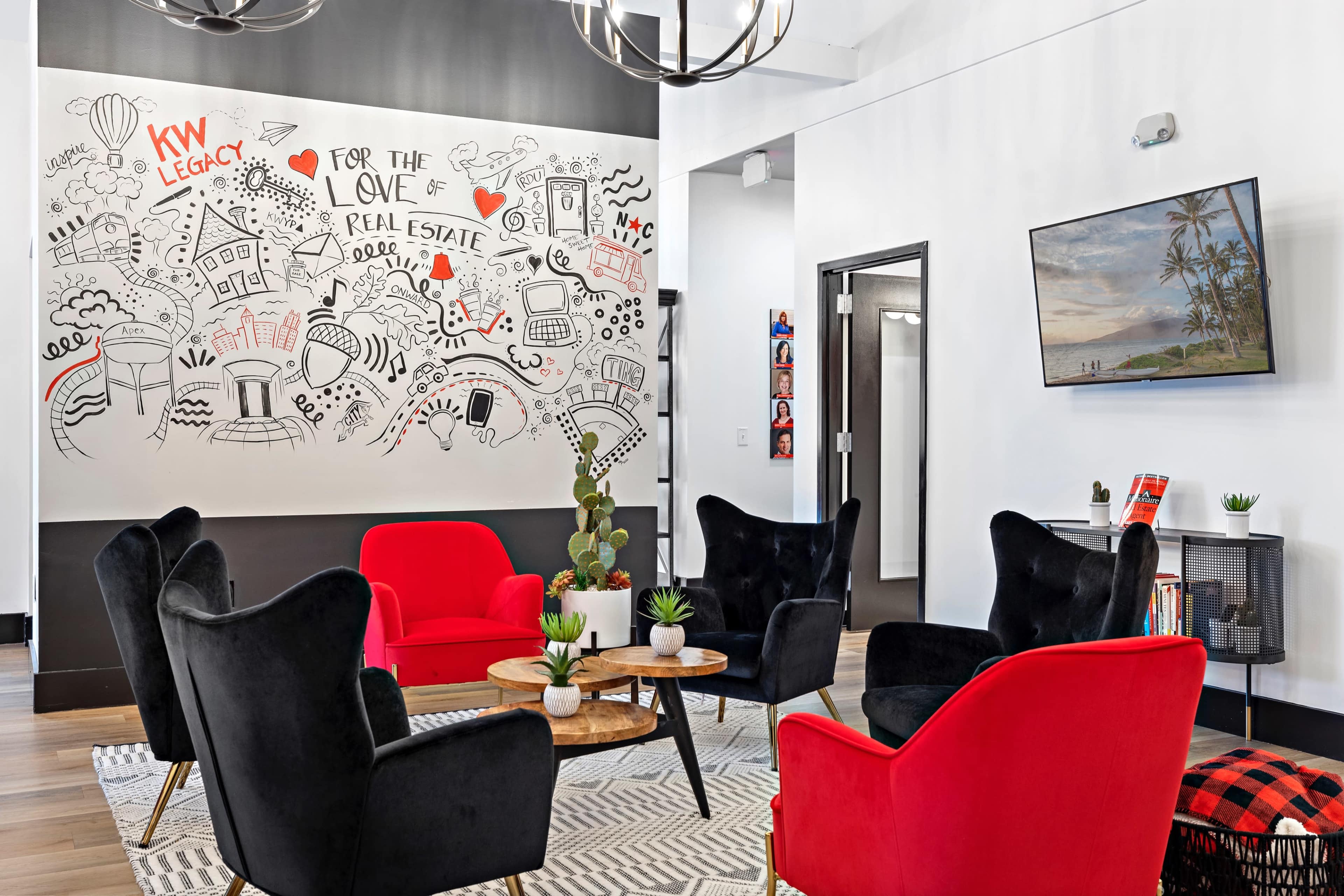 A modern office lounge area with red and black chairs arranged around wooden tables, featuring a large mural on the wall and a television mounted nearby.