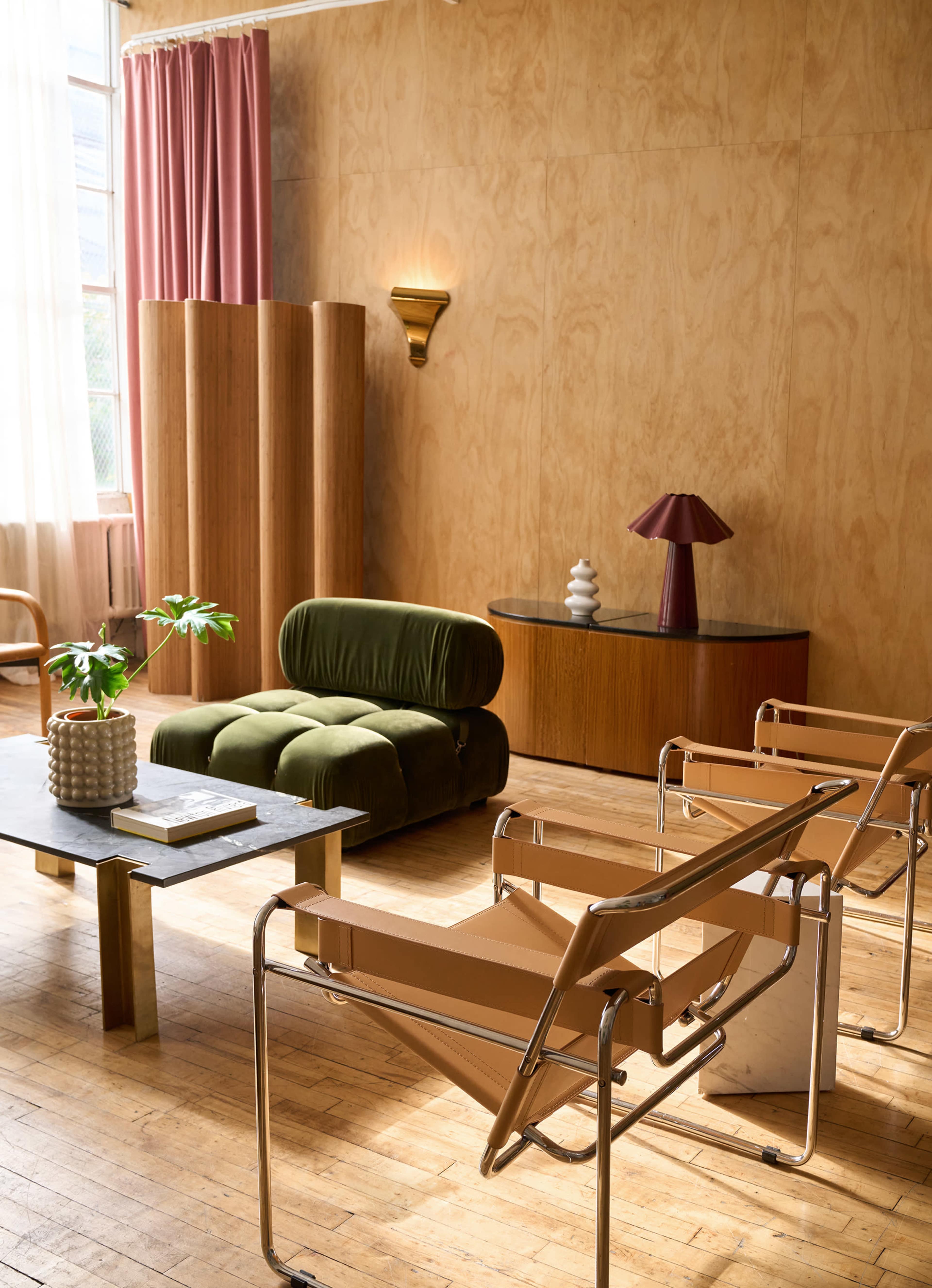 The image shows a modern living room with a green upholstered chair, beige lounge chairs, a dark coffee table, and wooden accents on the walls and furniture.