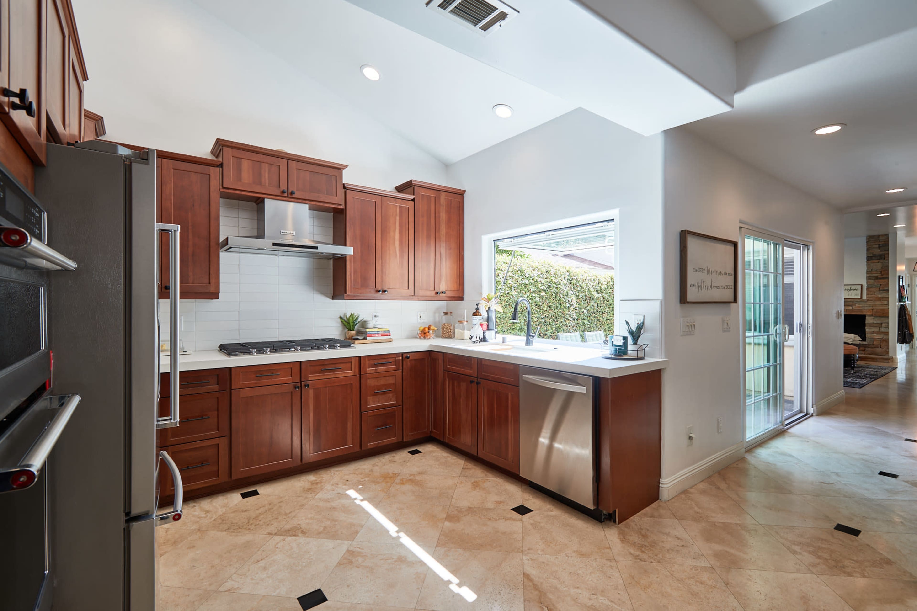 A modern kitchen with wooden cabinets, a stainless steel stove, and a large window overlooking greenery.