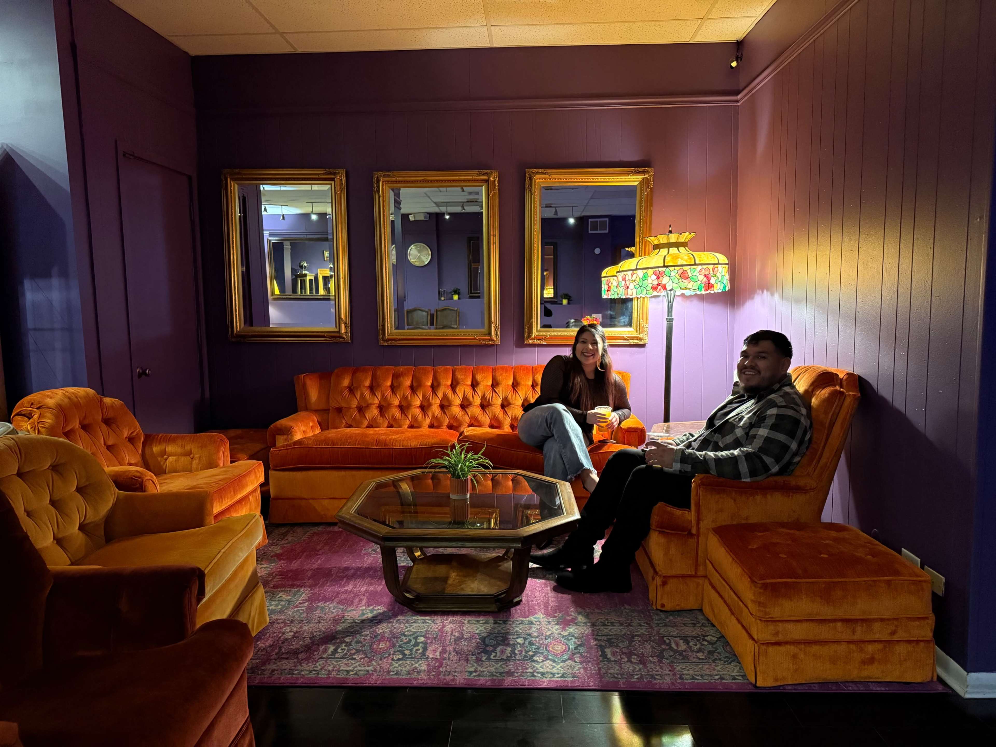 A cozy lounge area features a purple wall, orange velvet furniture, and decorative mirrors.