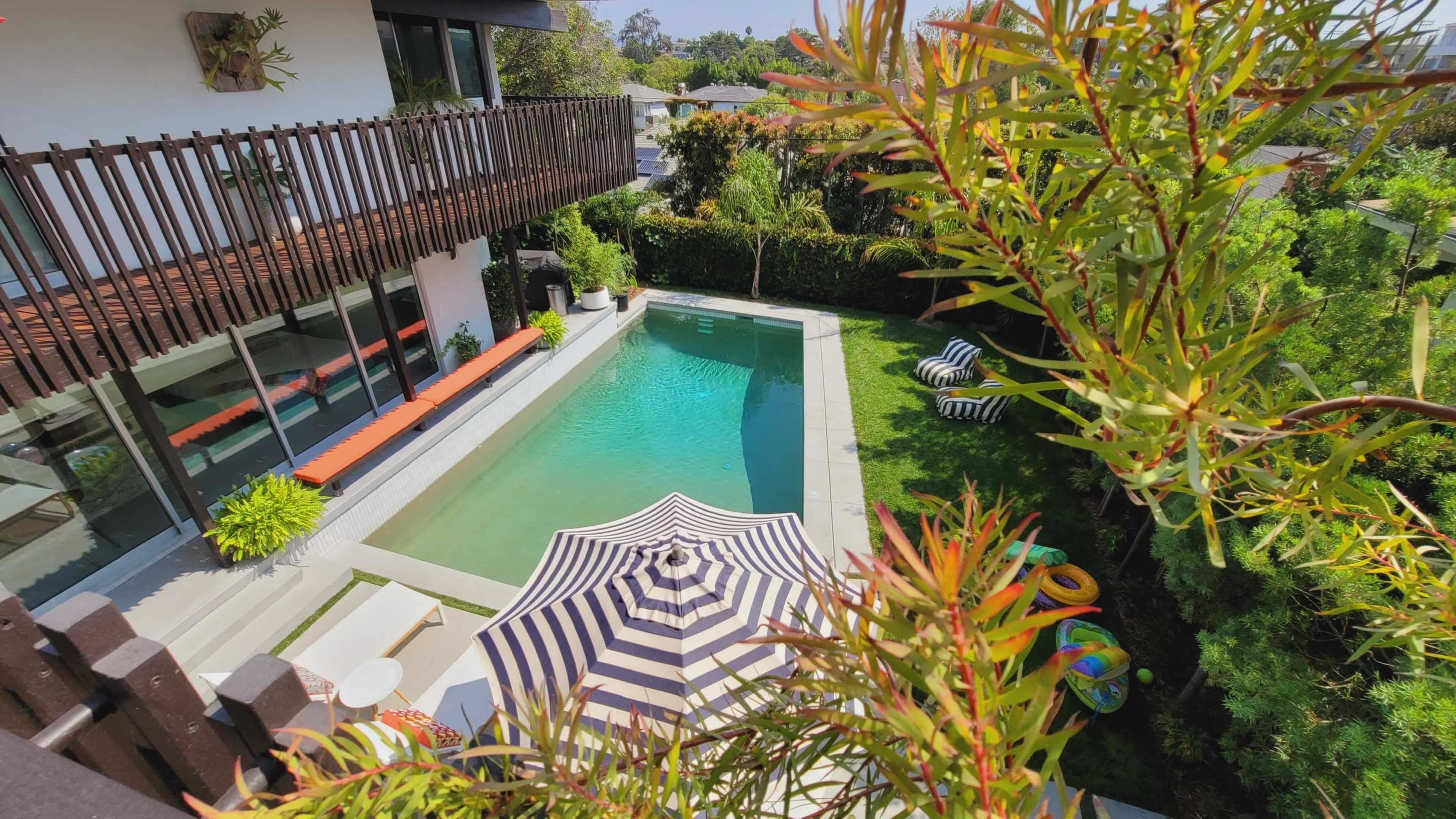 A modern house with a rectangular swimming pool and lounge area is surrounded by greenery and outdoor seating.