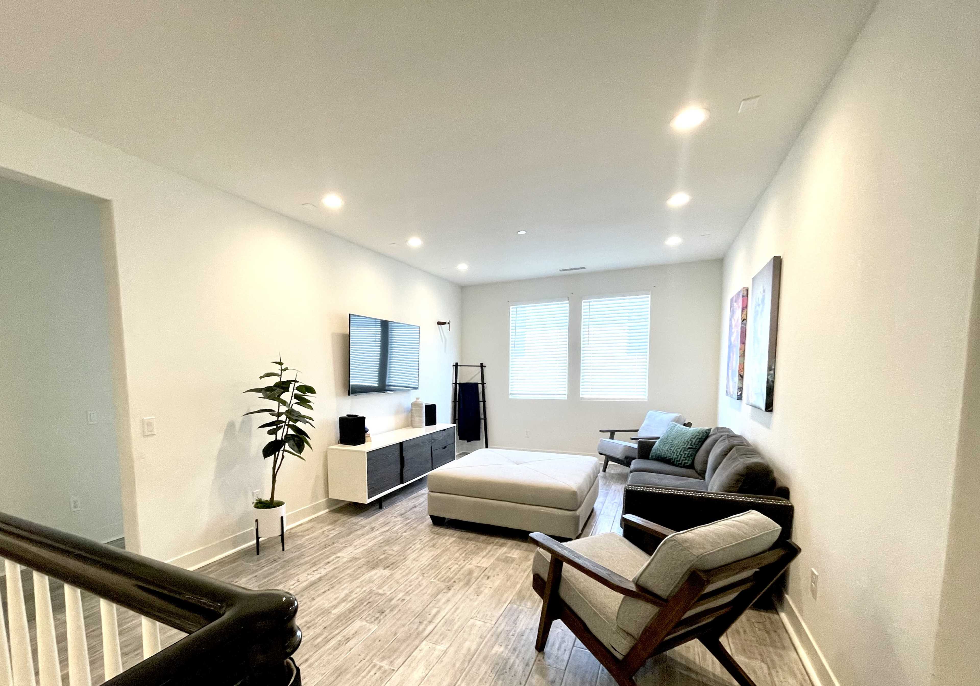 A modern living room with a sectional sofa, a television mounted on the wall, and a light-colored rug on the floor.