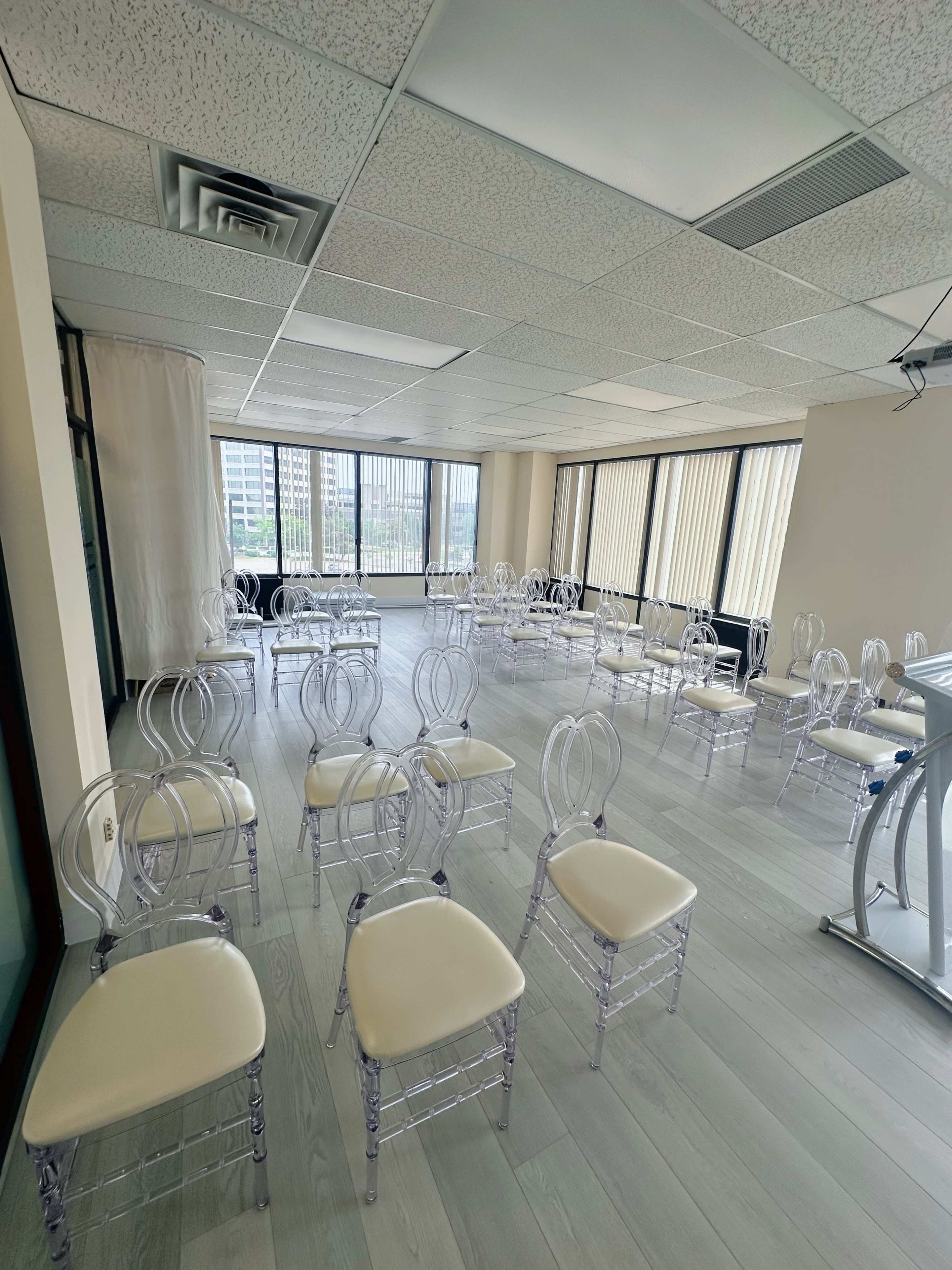 The image shows a spacious room with numerous clear plastic chairs arranged in rows, awaiting an event.