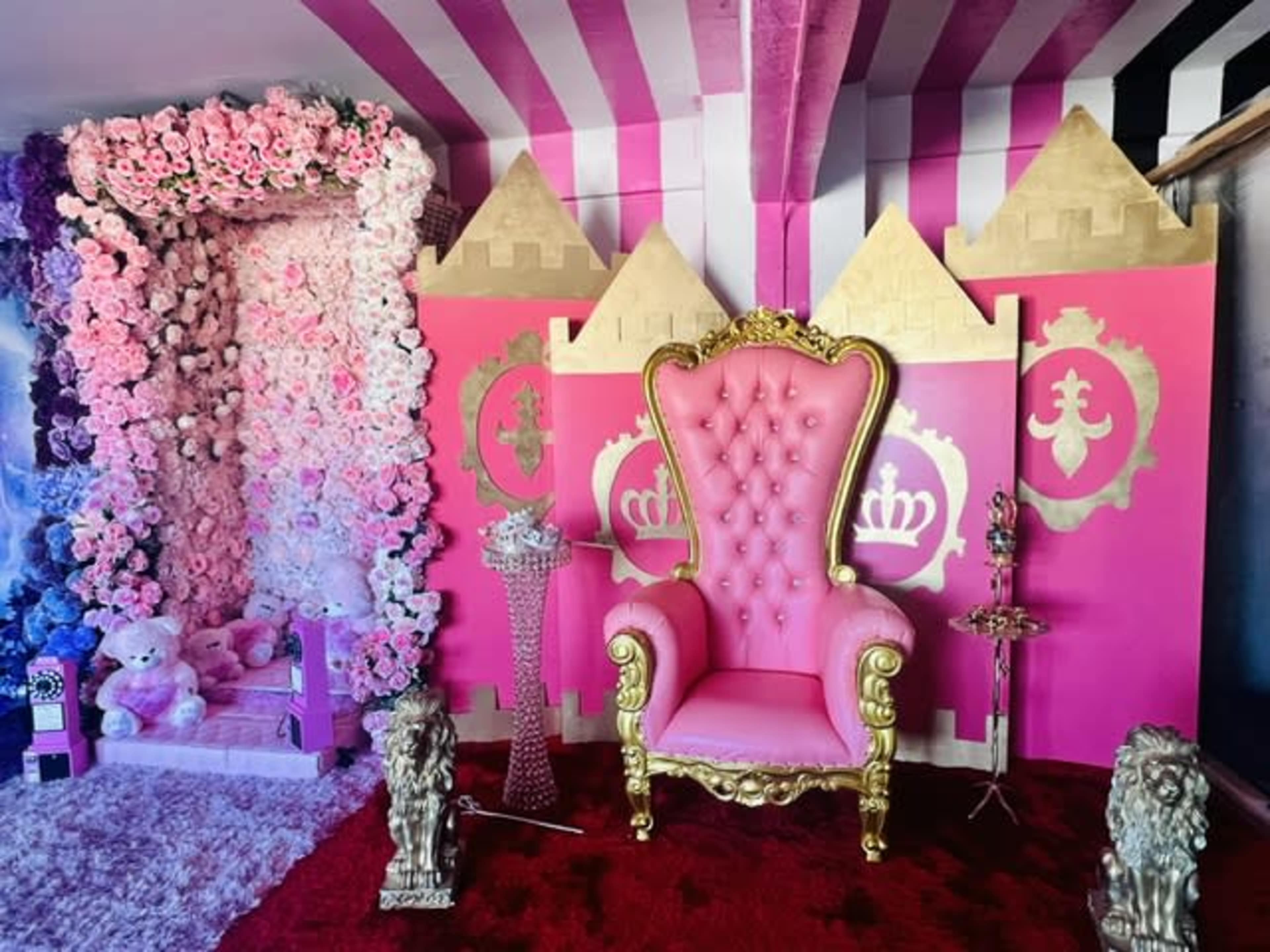 The scene features a pink throne surrounded by a floral backdrop and decorative castle walls, with plush toys and ornate statues.