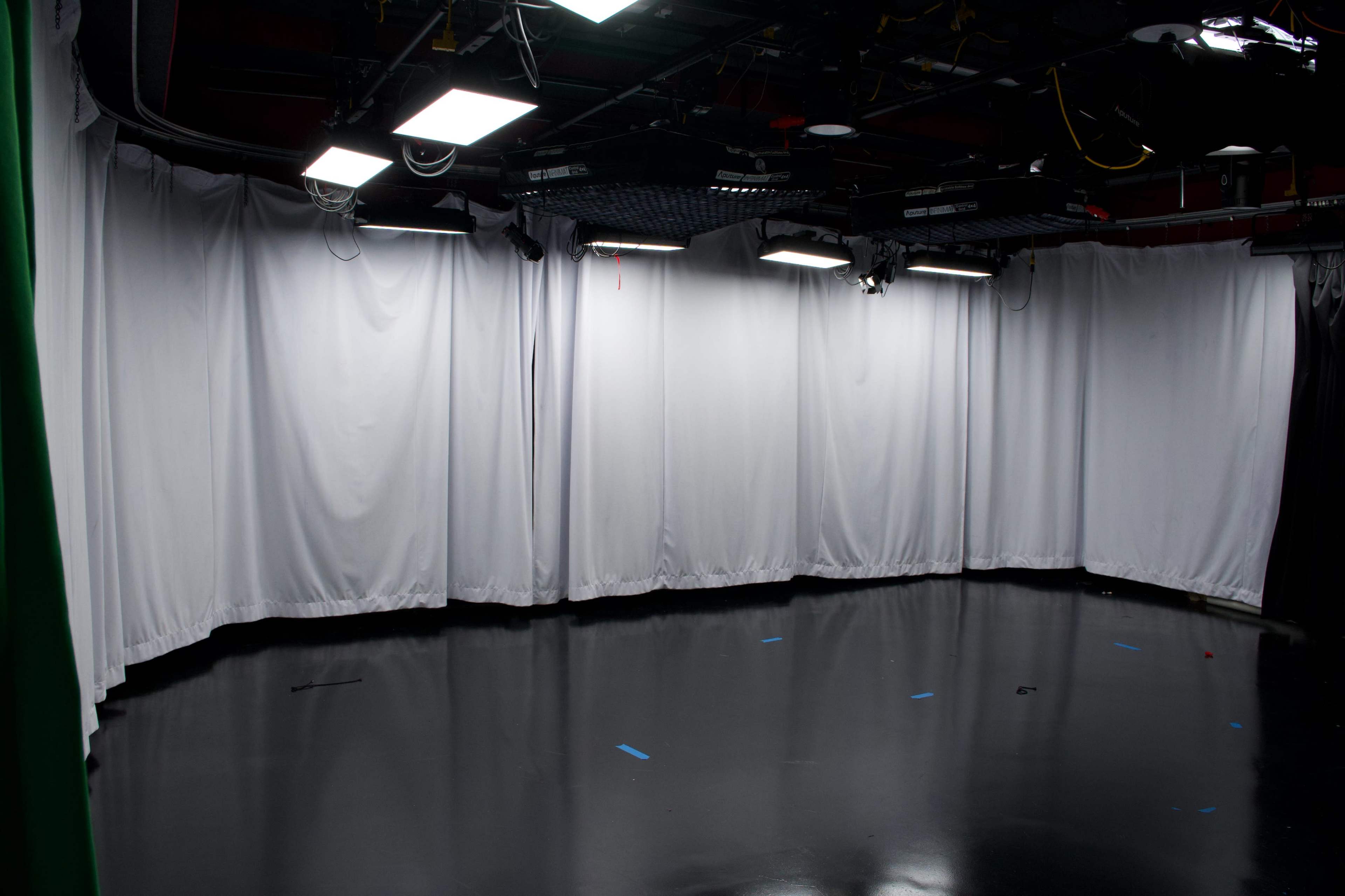 The image shows a television studio with white curtains and a glossy black floor, equipped with overhead lighting.
