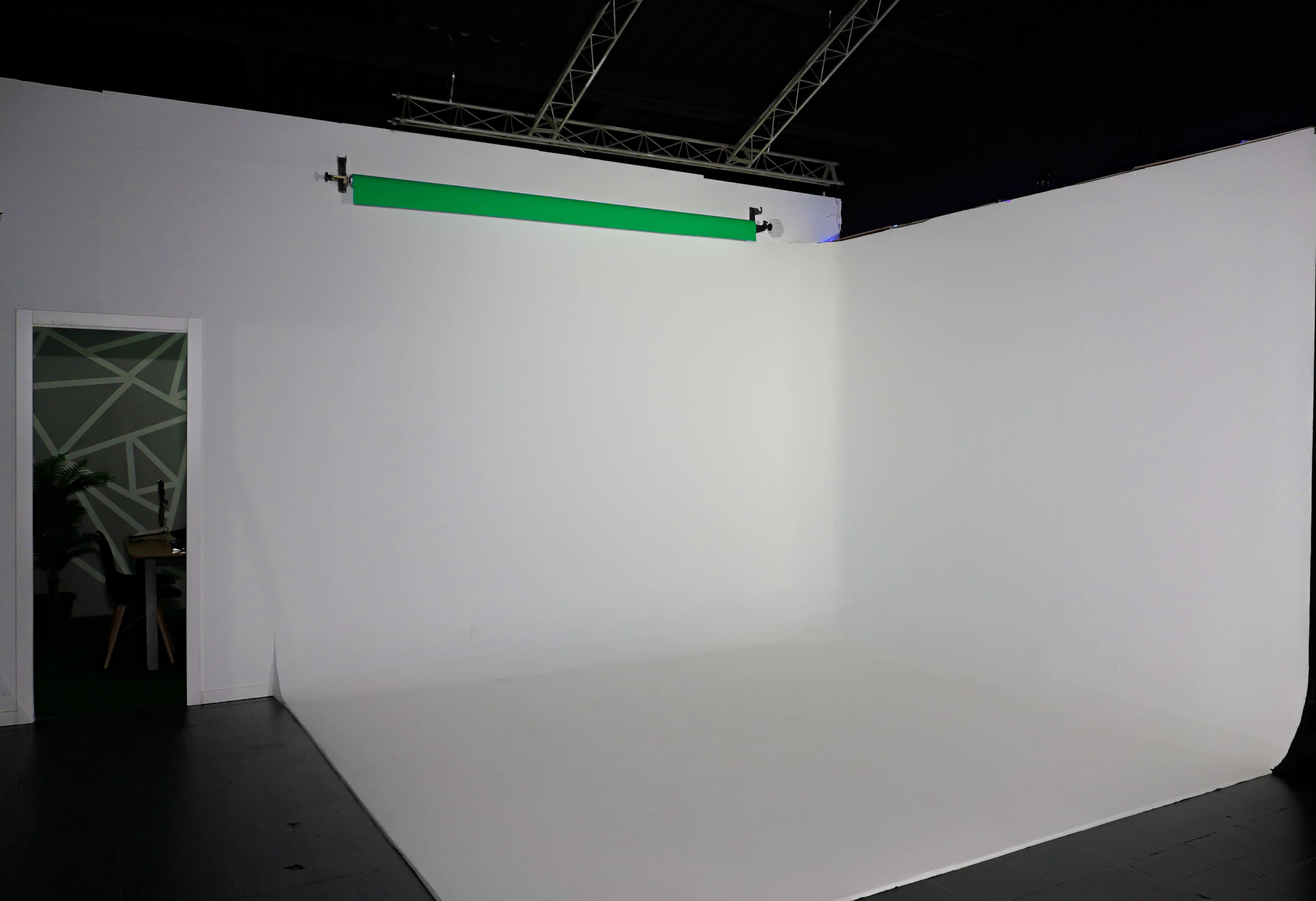The image shows a blank white photo studio with a doorway and a green backdrop mount at the top.