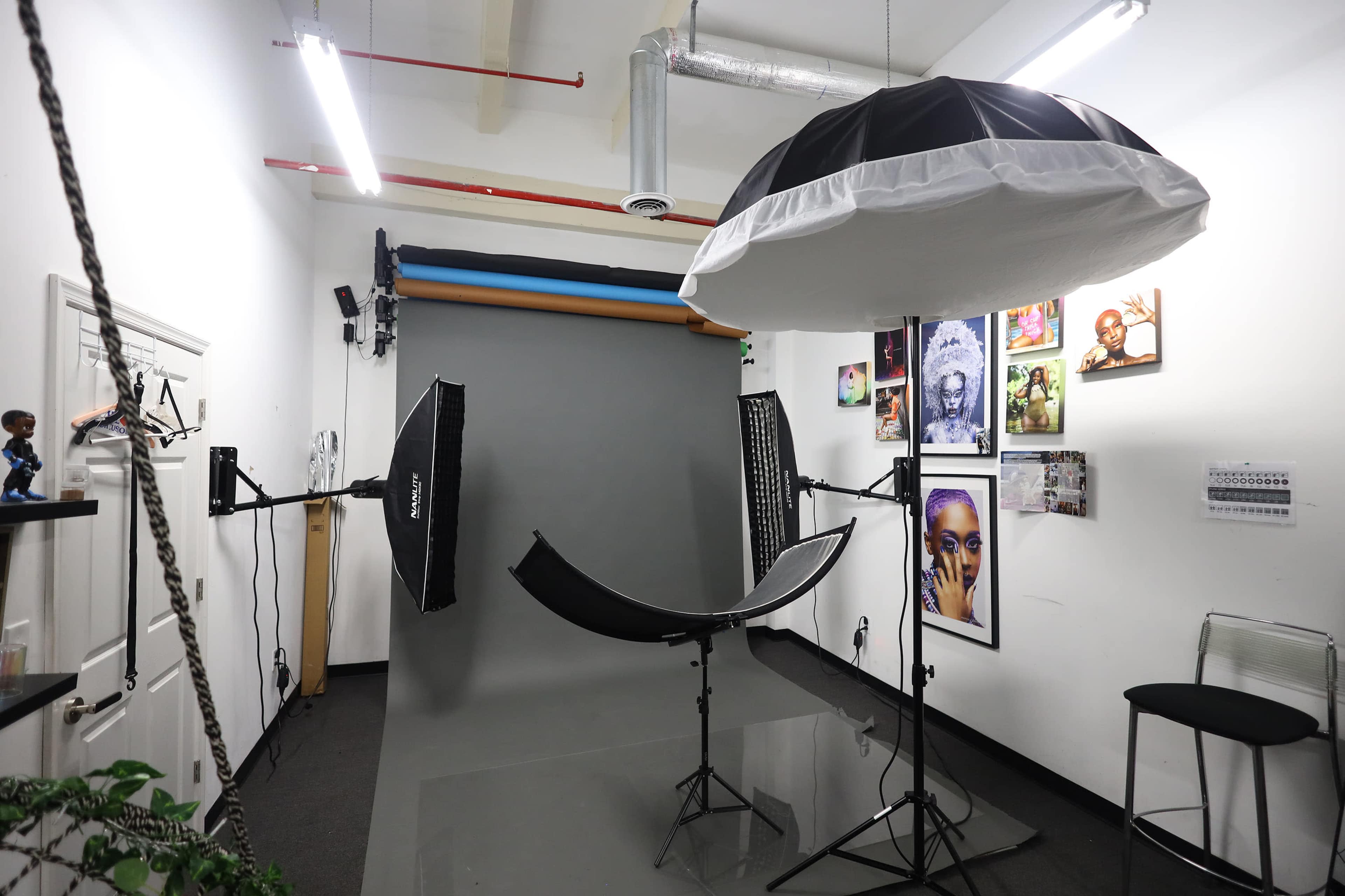 The image shows a photography studio with a gray backdrop, lighting equipment, and a large softbox overhead.