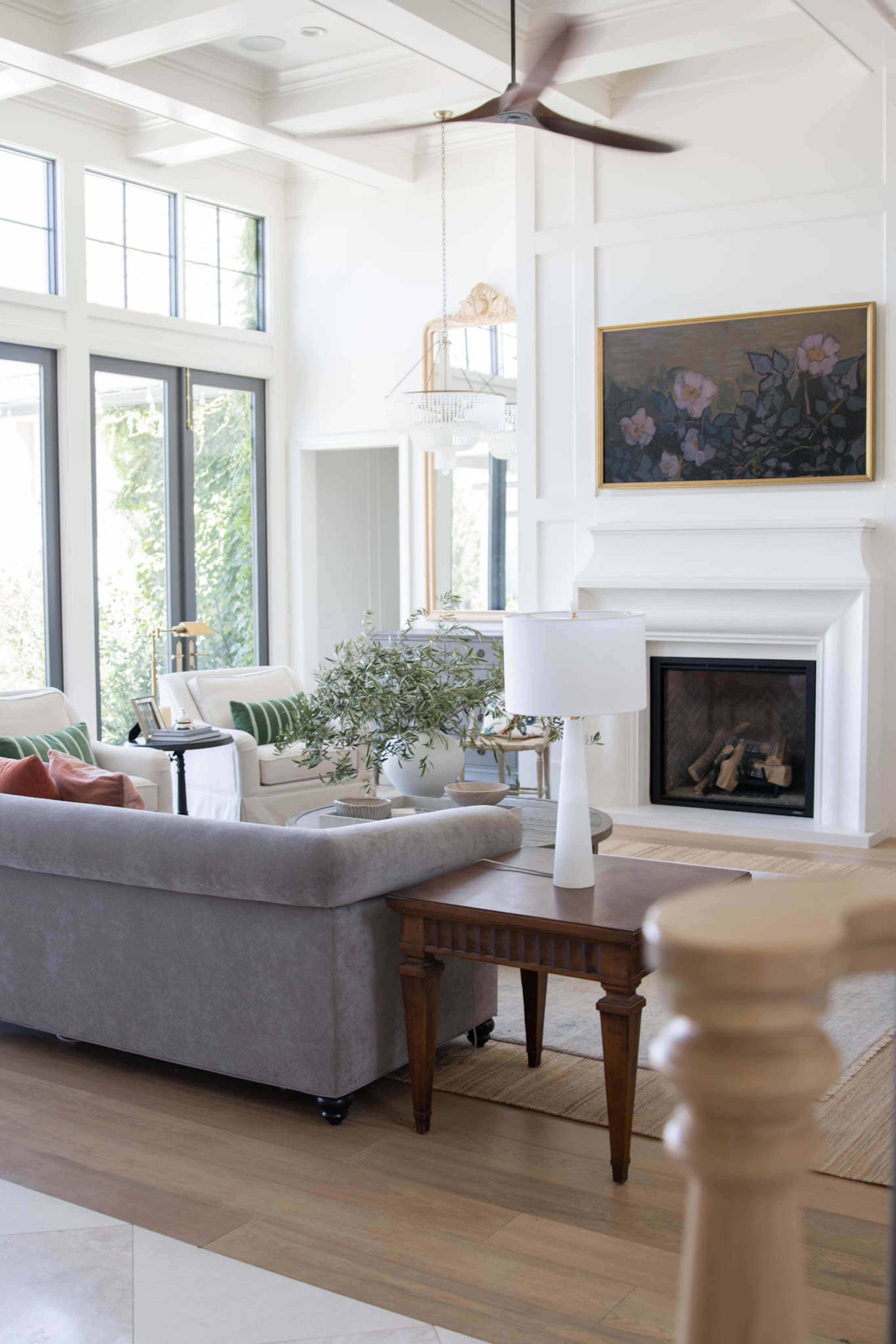 The image depicts a bright, open living room with a gray couch, wooden coffee table, and large windows that allow natural light to fill the space.