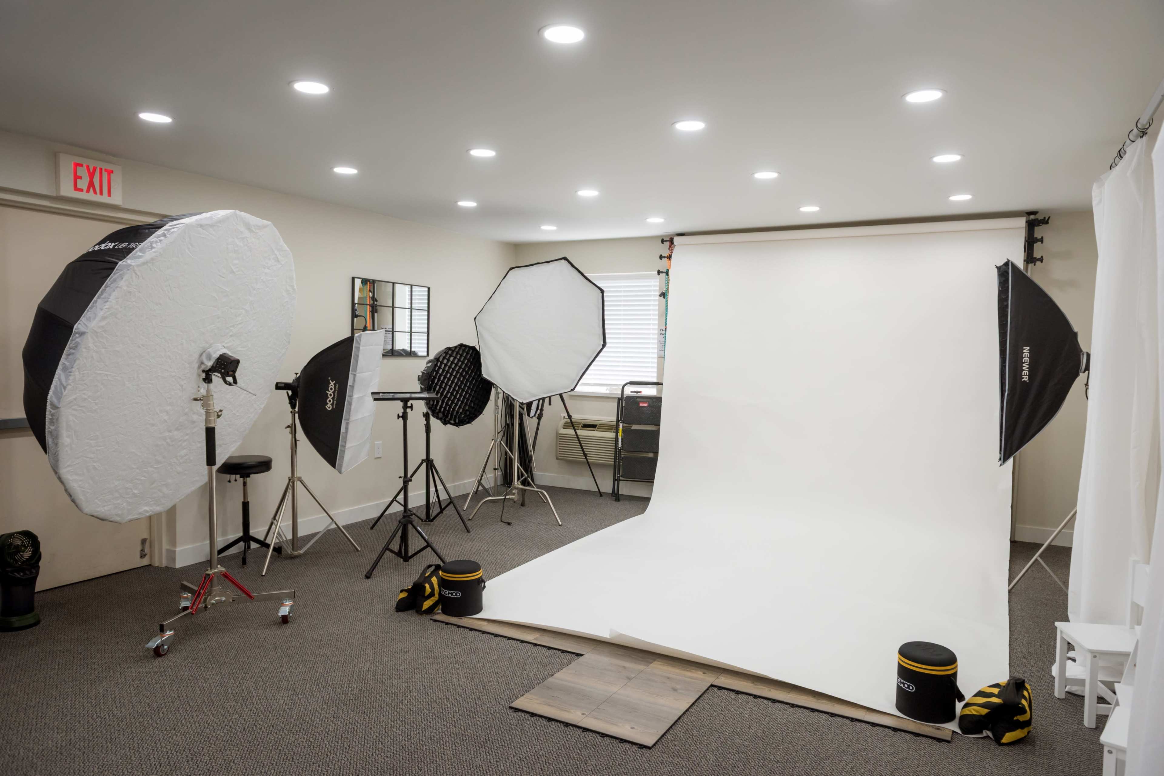 The image shows a photography studio equipped with several lighting setups, a blank backdrop, and various props arranged in a well-lit room.