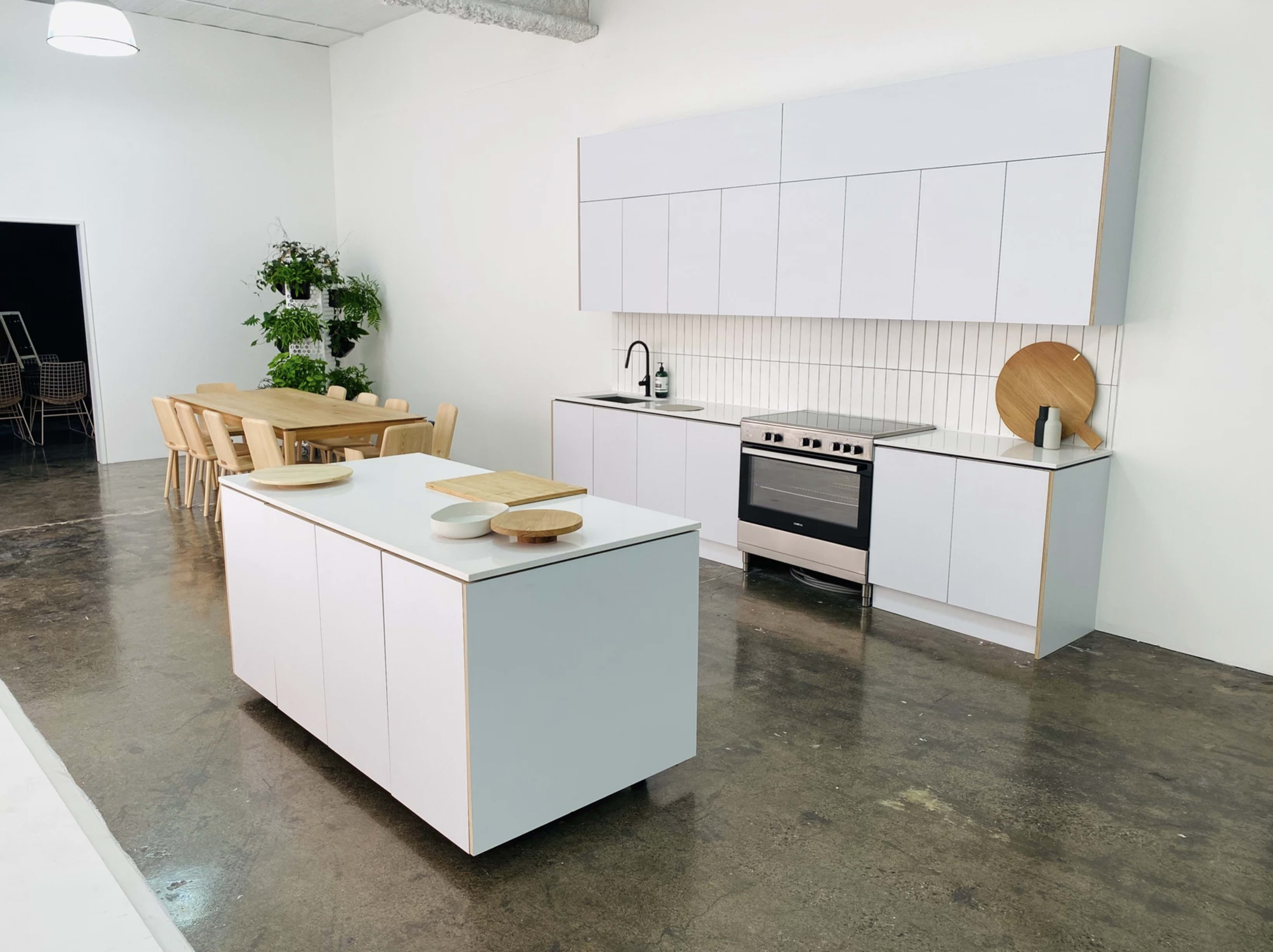 A modern kitchen with a white cabinetry setup, an island in the center, a stainless steel oven, and a dining table with wooden chairs.