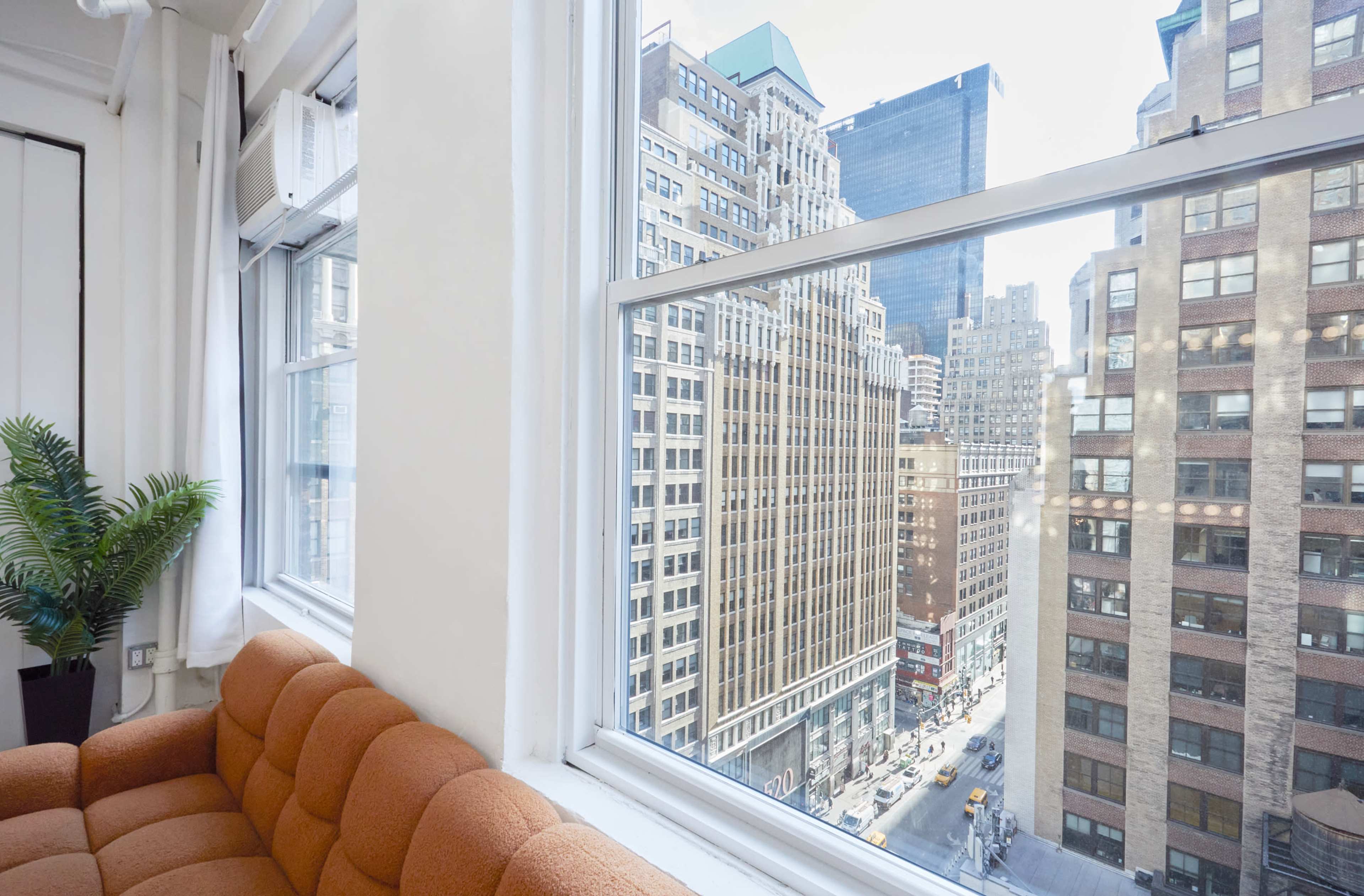 A view of a cityscape featuring tall buildings and streets, seen through a large window beside a brown couch.