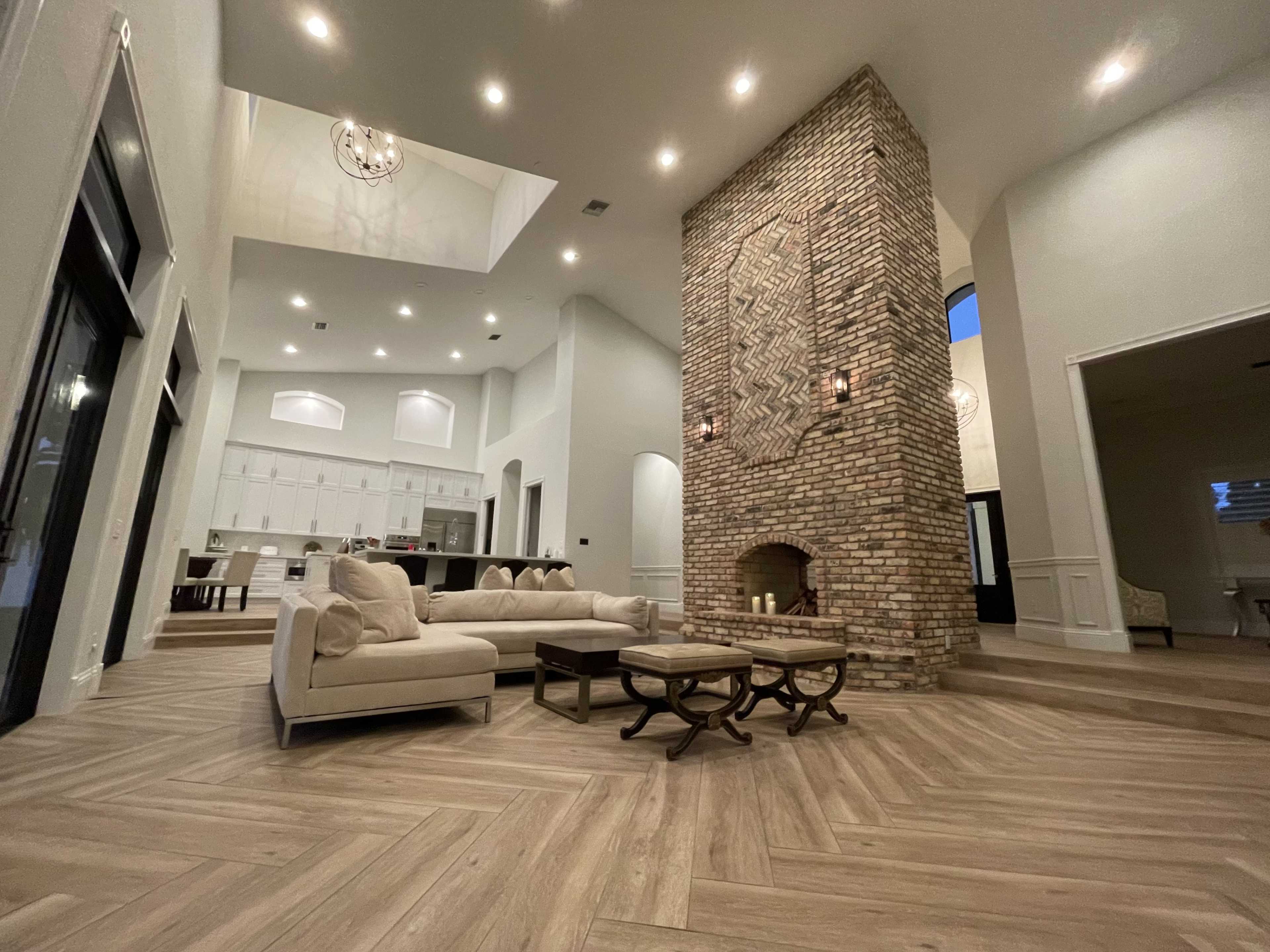 A modern living room with a large brick fireplace, a sectional sofa, and a view into a kitchen area in the background.