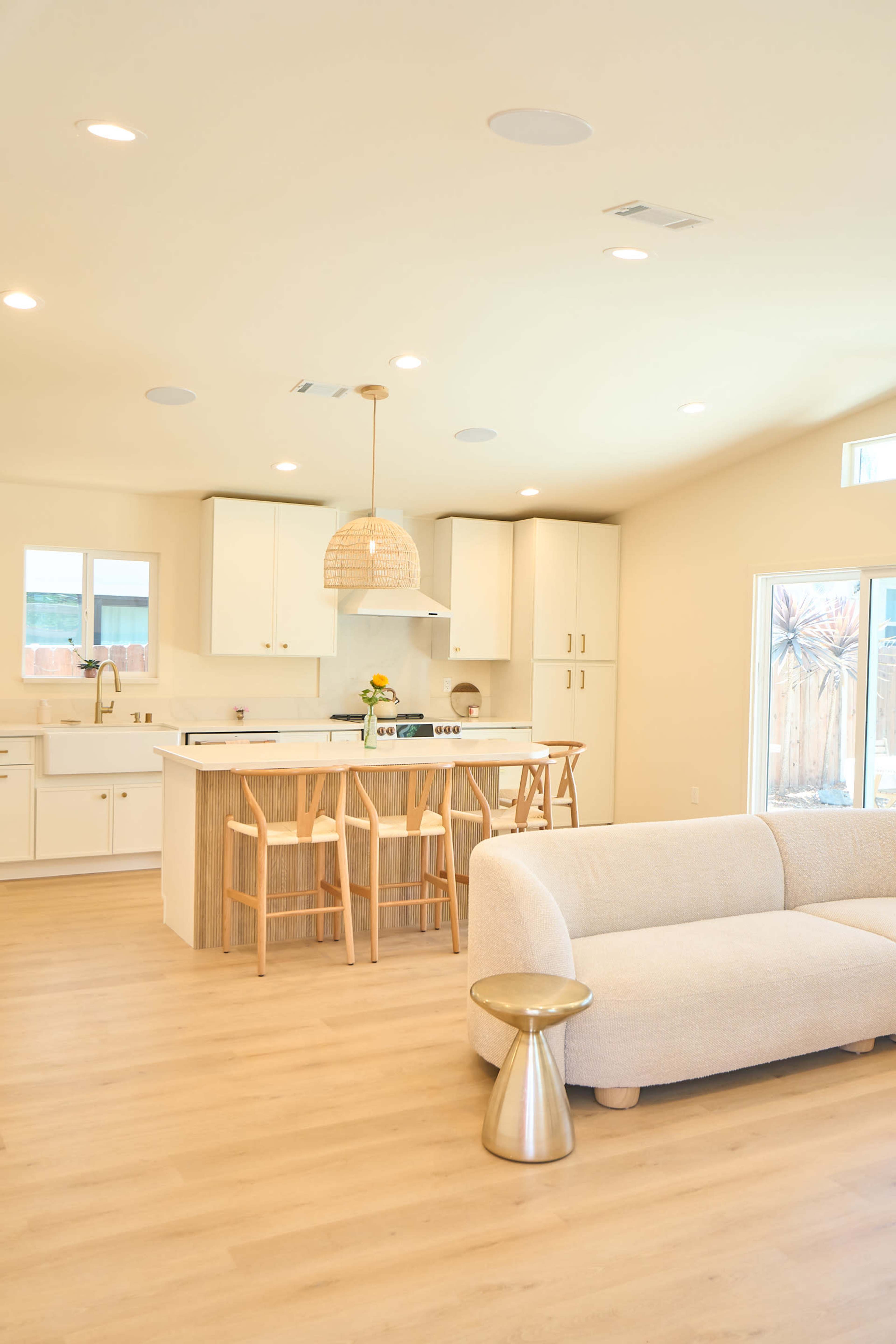 The image features a modern, open-concept kitchen and living area with a light color palette, wooden accents, and minimalistic furniture.