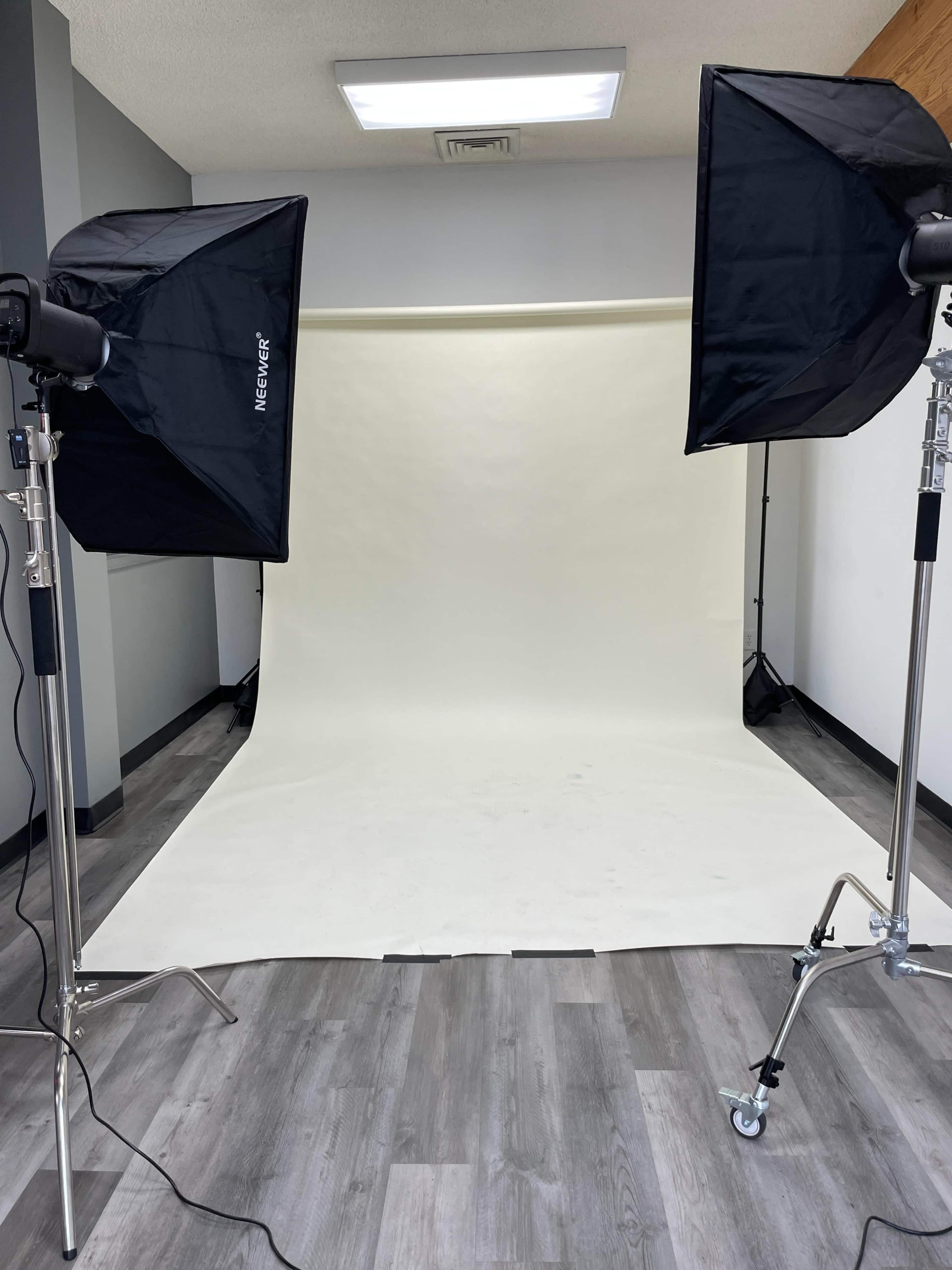 A photography studio setup with two softbox lights and a plain backdrop.