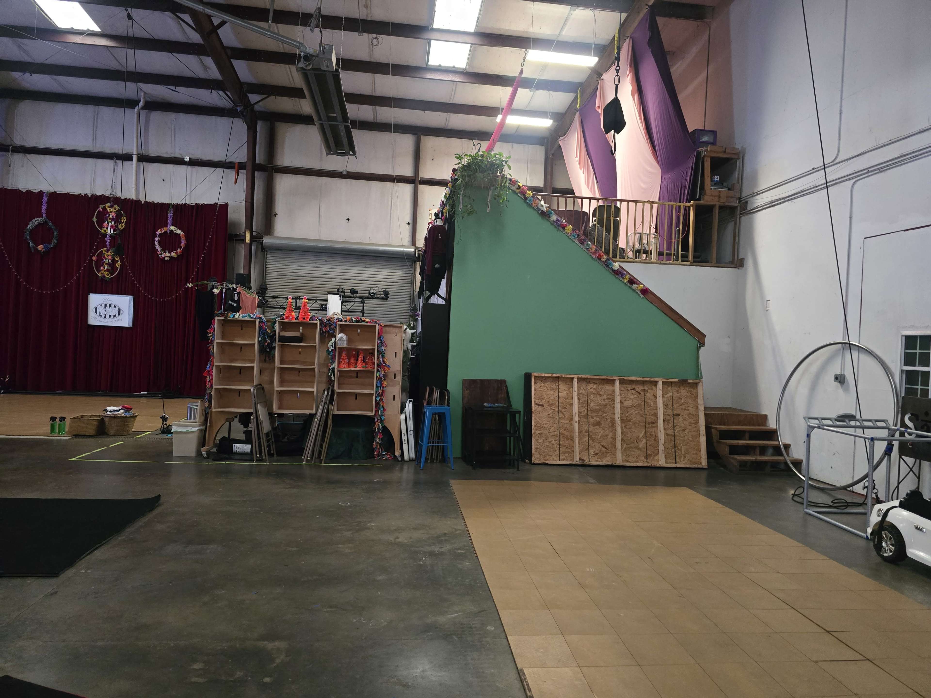 An indoor space with a green staircase on the right, shelves and equipment against the walls, and a large open floor area in front.