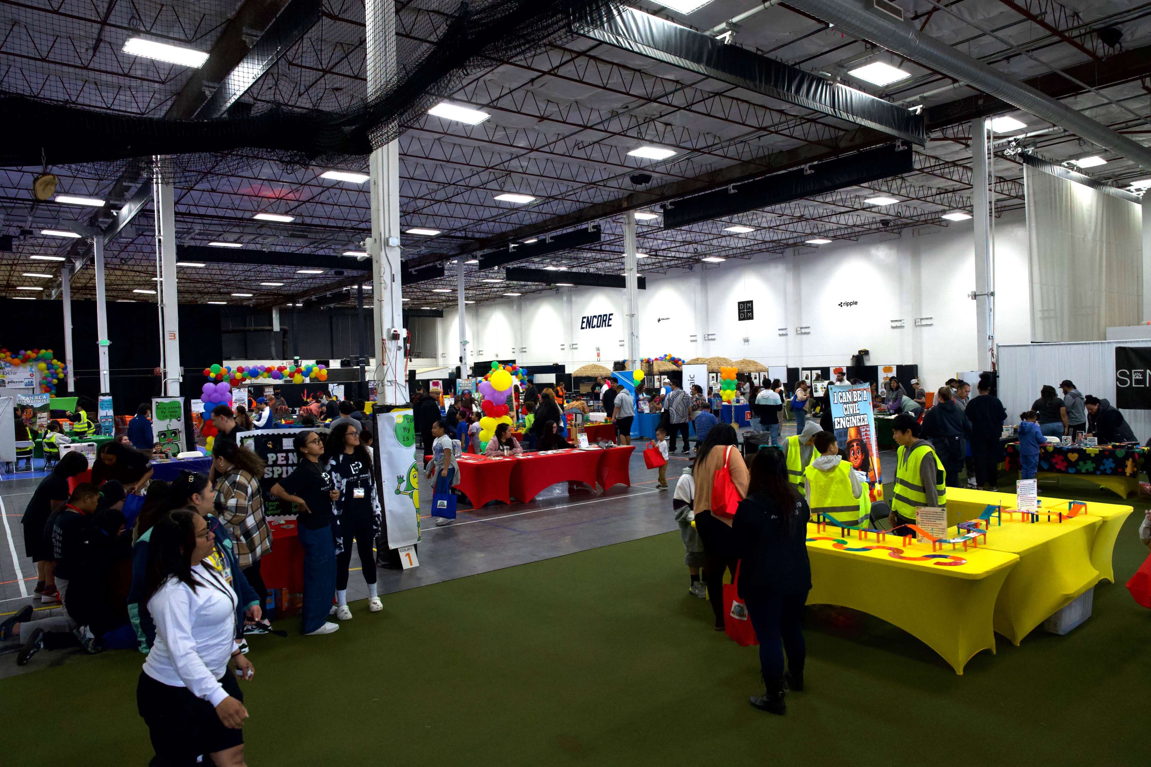 A large indoor space filled with booths and tables, where people engage in various activities and games during an event.