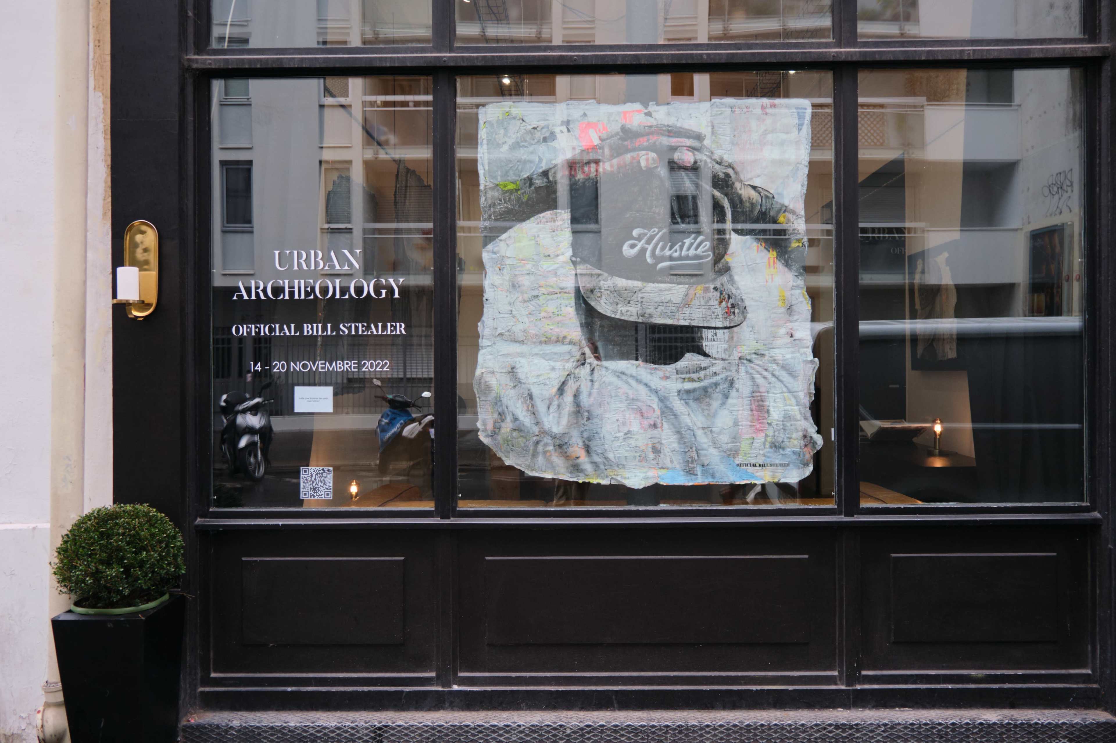 The image shows a window display with a poster featuring a hat and the word "Hustle," accompanied by details about an event titled "Urban Archeology."