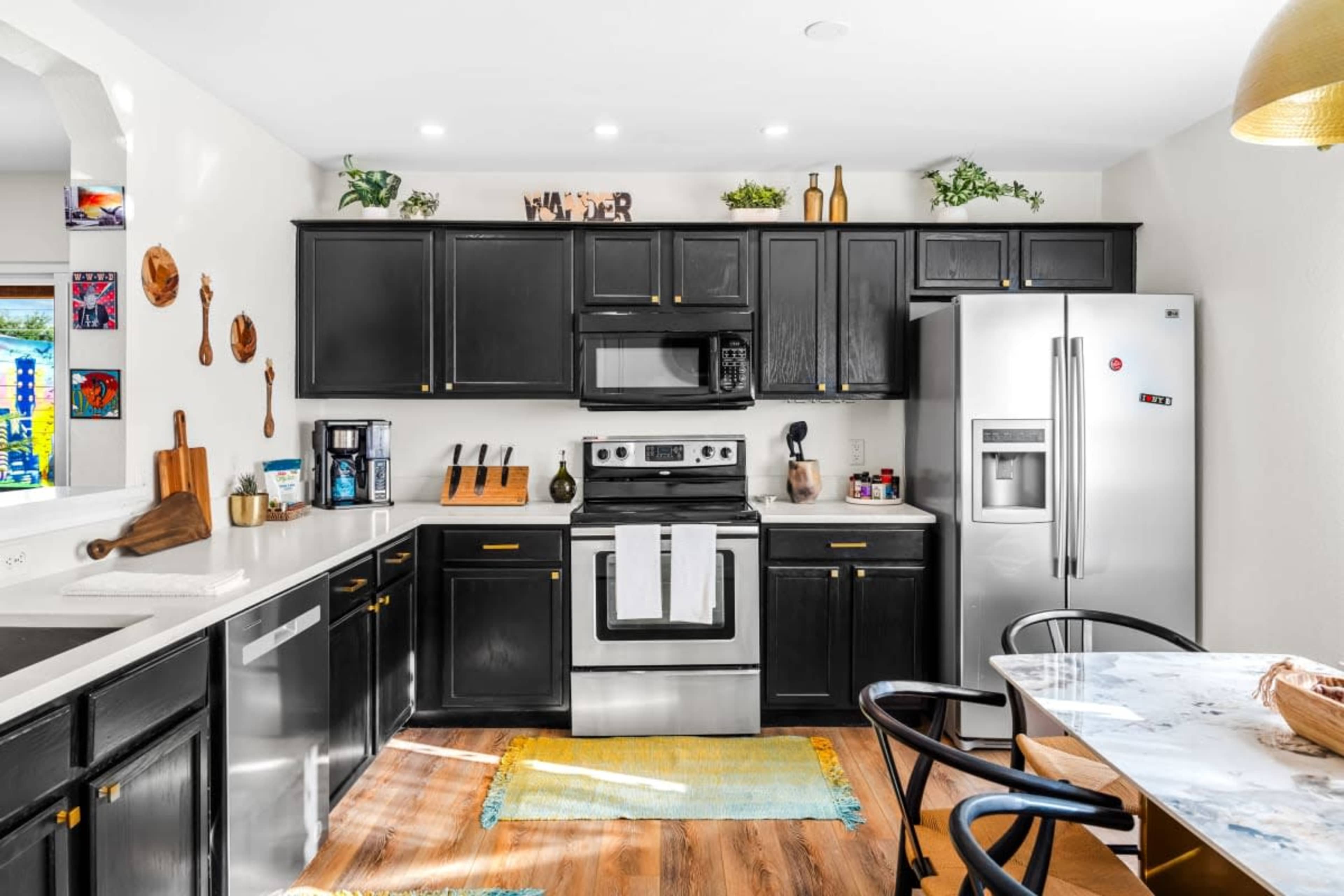 The kitchen features dark cabinetry, stainless steel appliances, and a light-colored countertop with wooden utensils displayed on the walls.