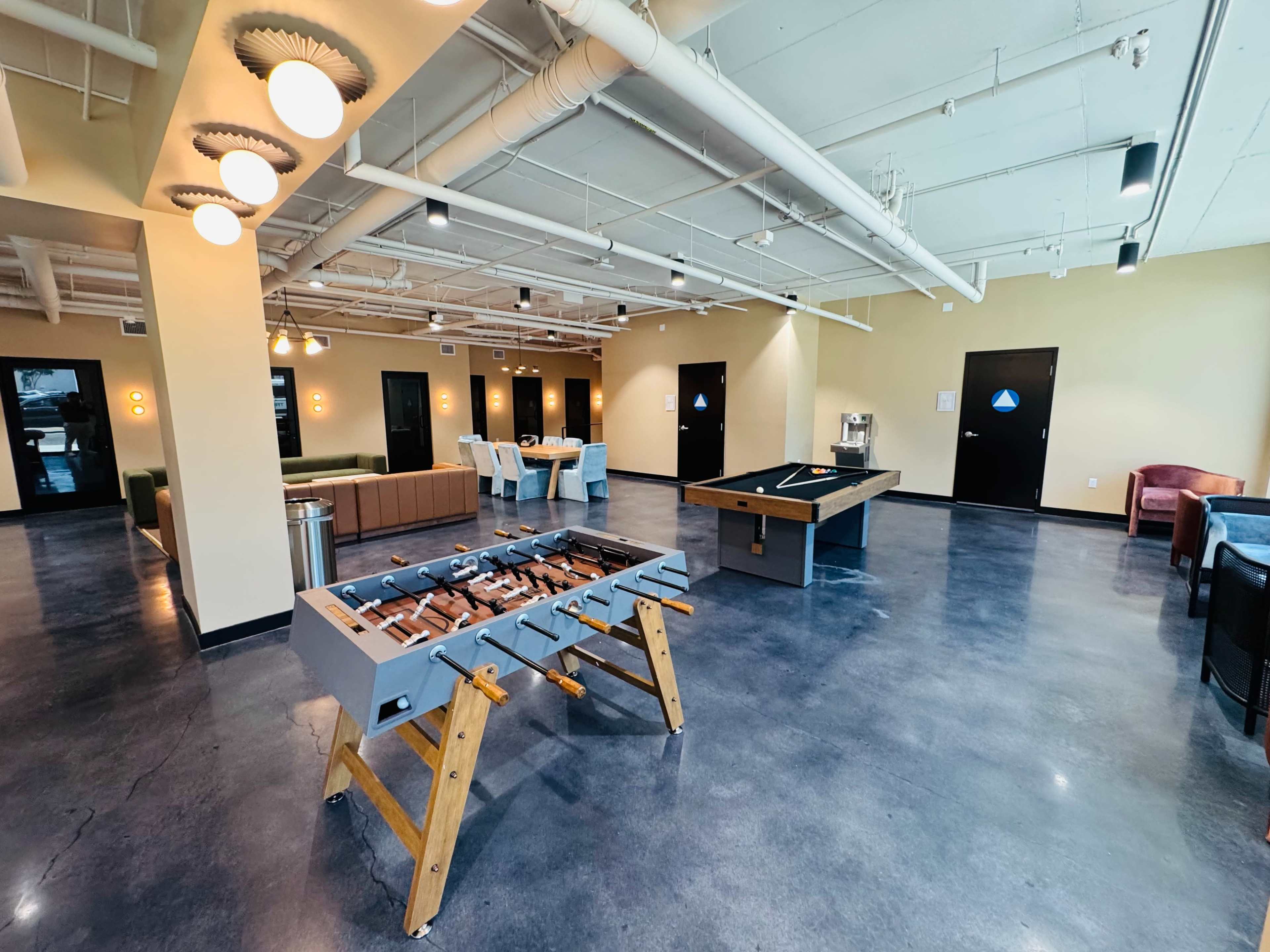 The image shows a spacious indoor recreation area with a foosball table, a pool table, and various seating arrangements.
