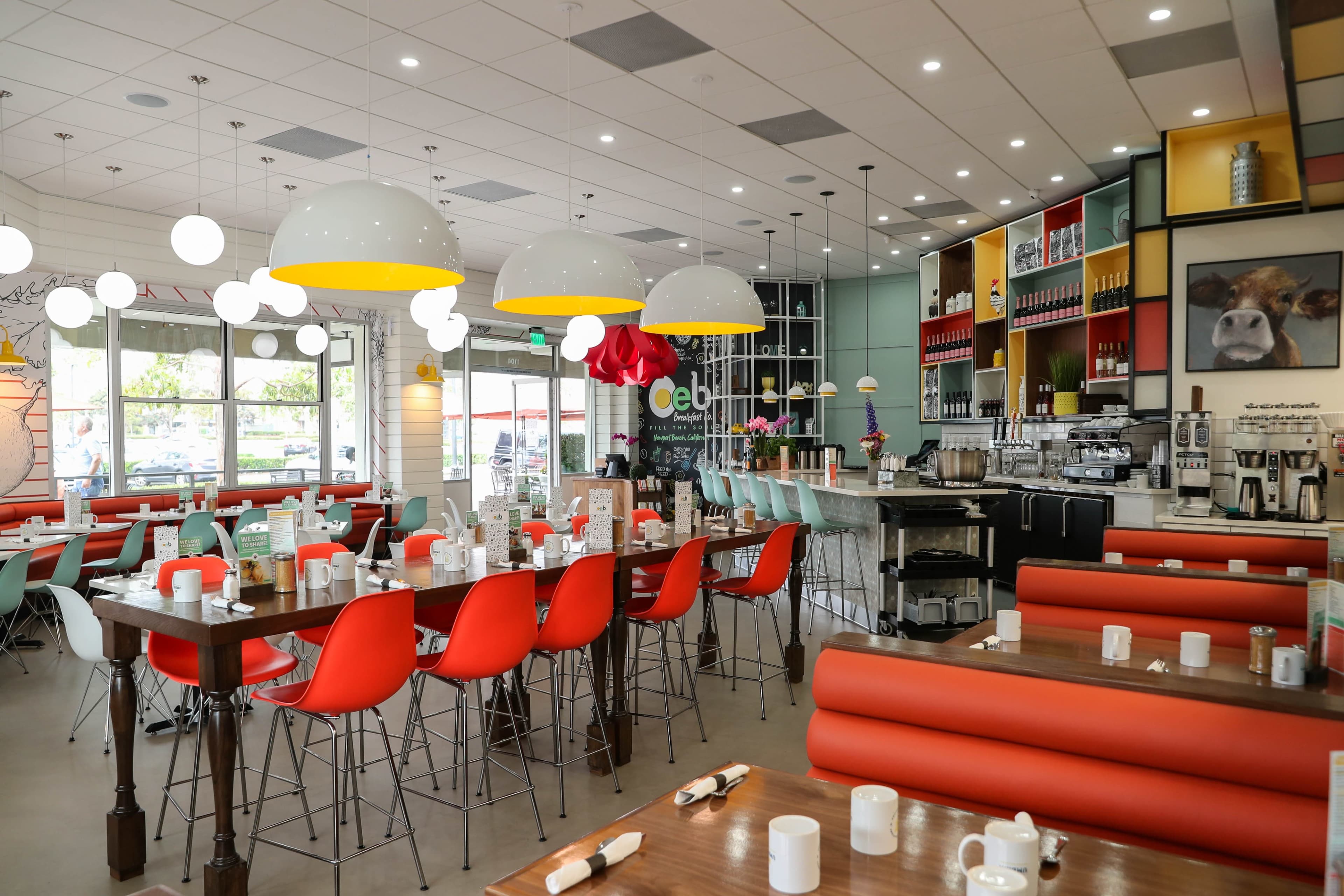 A modern restaurant interior with colorful seating, hanging light fixtures, and a coffee bar along one side.