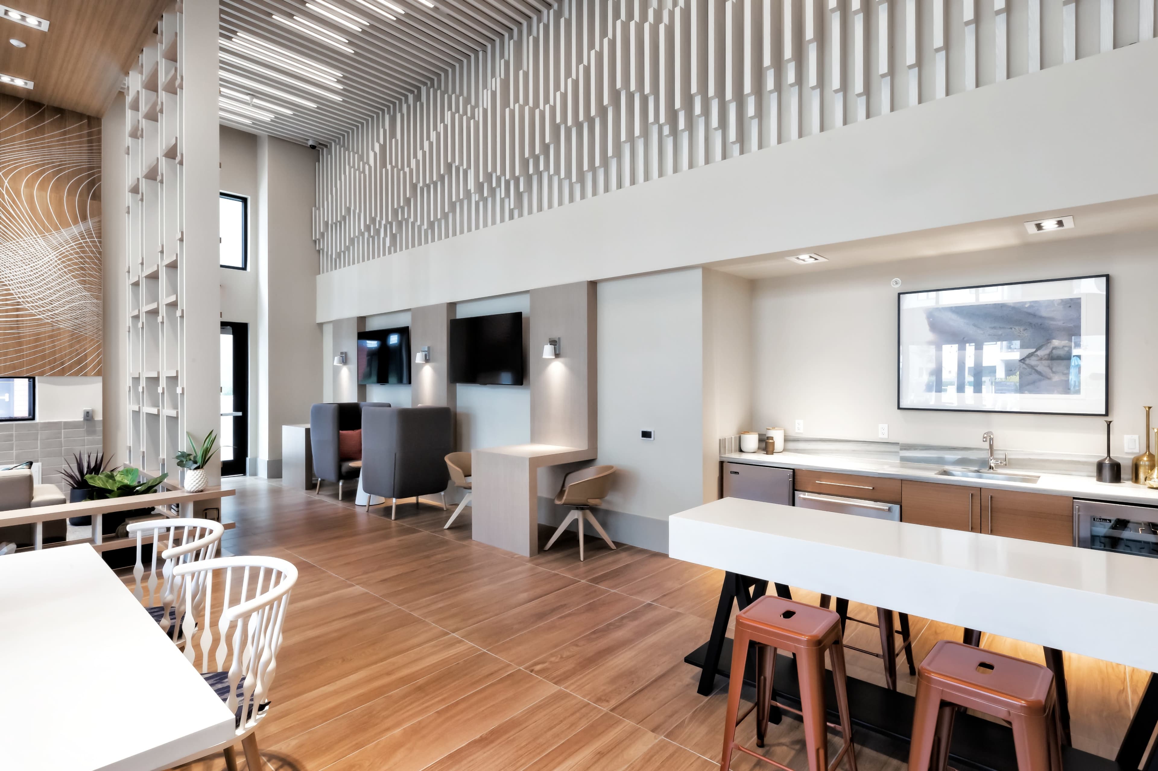 A modern communal kitchen and lounge area with wooden flooring, stylish seating, and large windows.