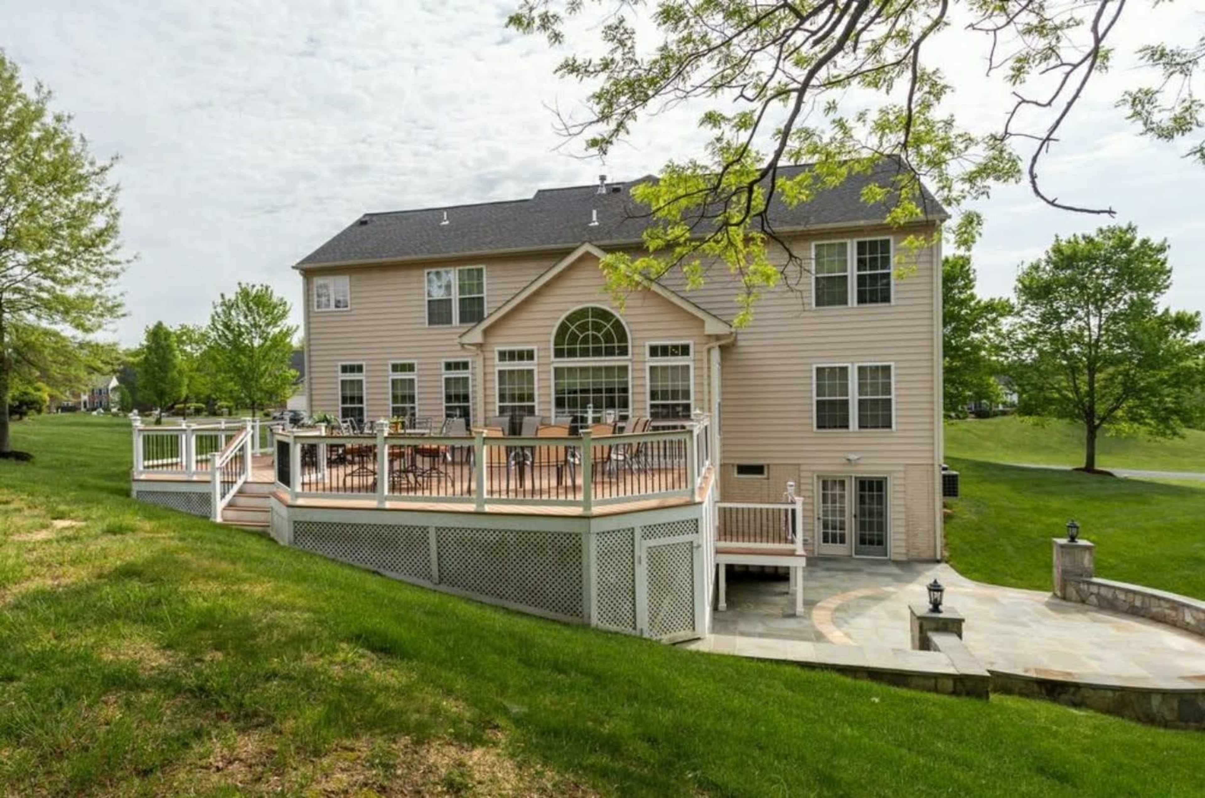 A large two-story house with a deck overlooking a grassy area.