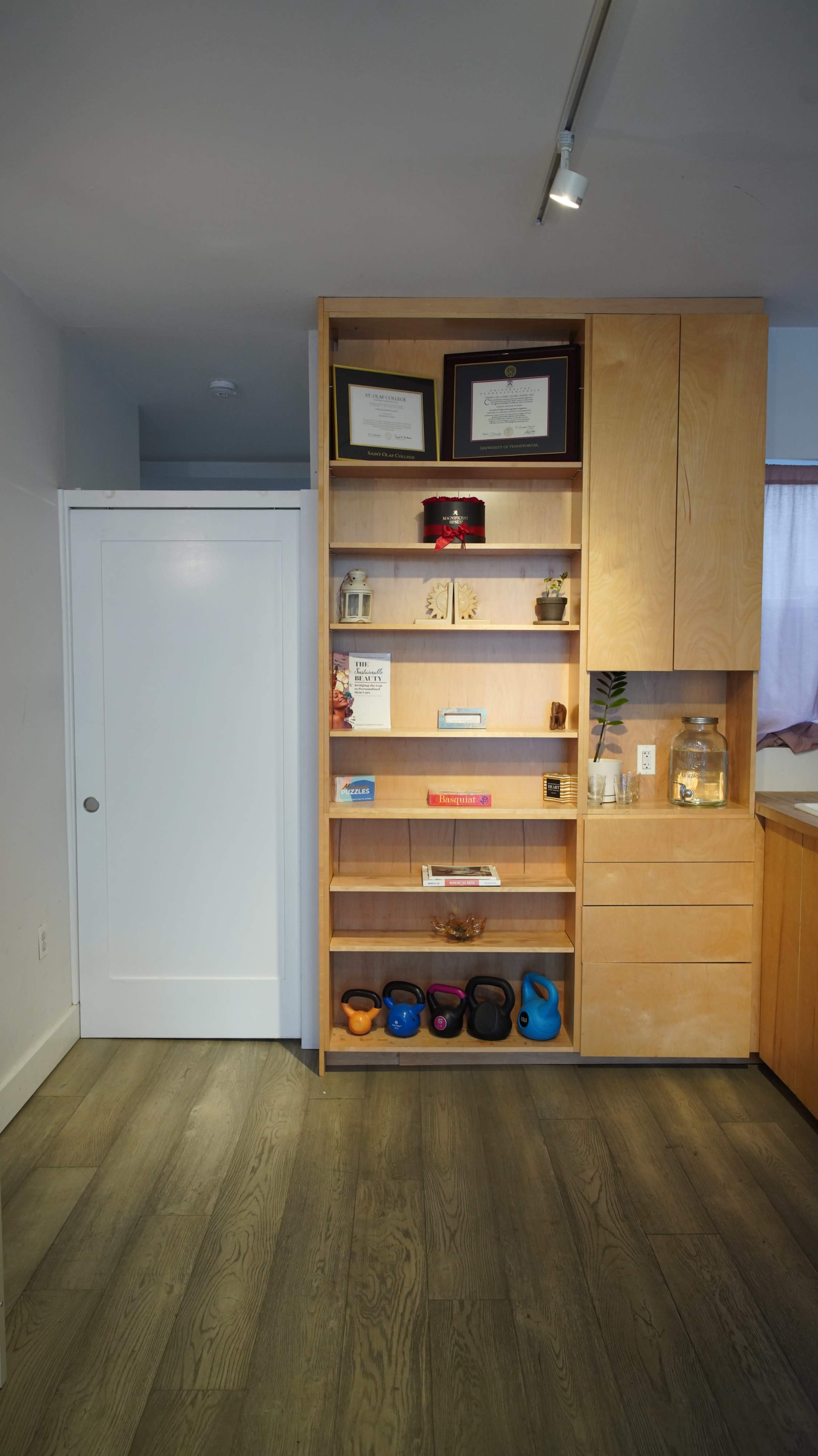 The image features a wooden shelving unit with various items and awards arranged on it, alongside a closed white door in a room with hardwood flooring.