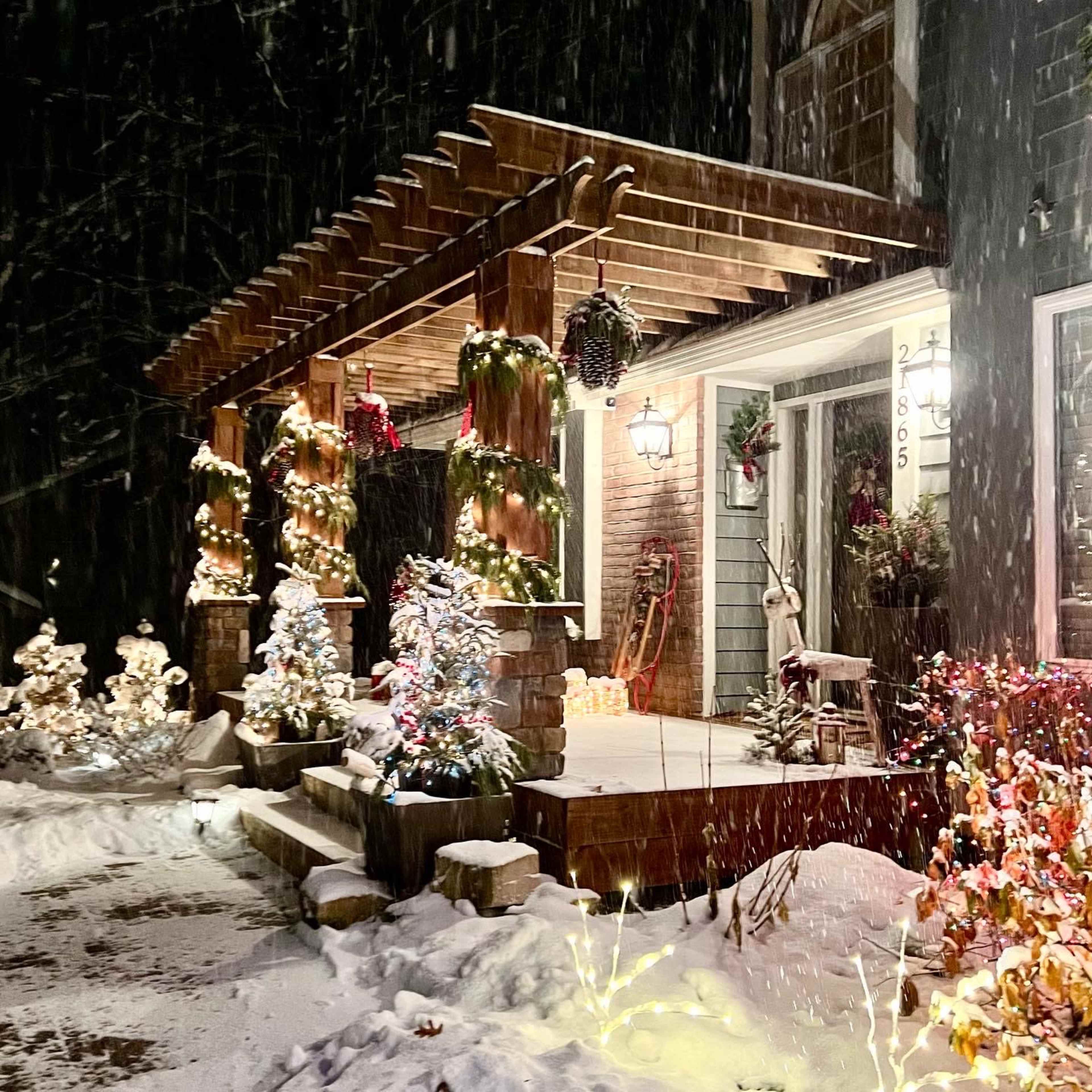 A snow-covered porch adorned with festive lights and decorations stands illuminated against a dark, snowy backdrop.
