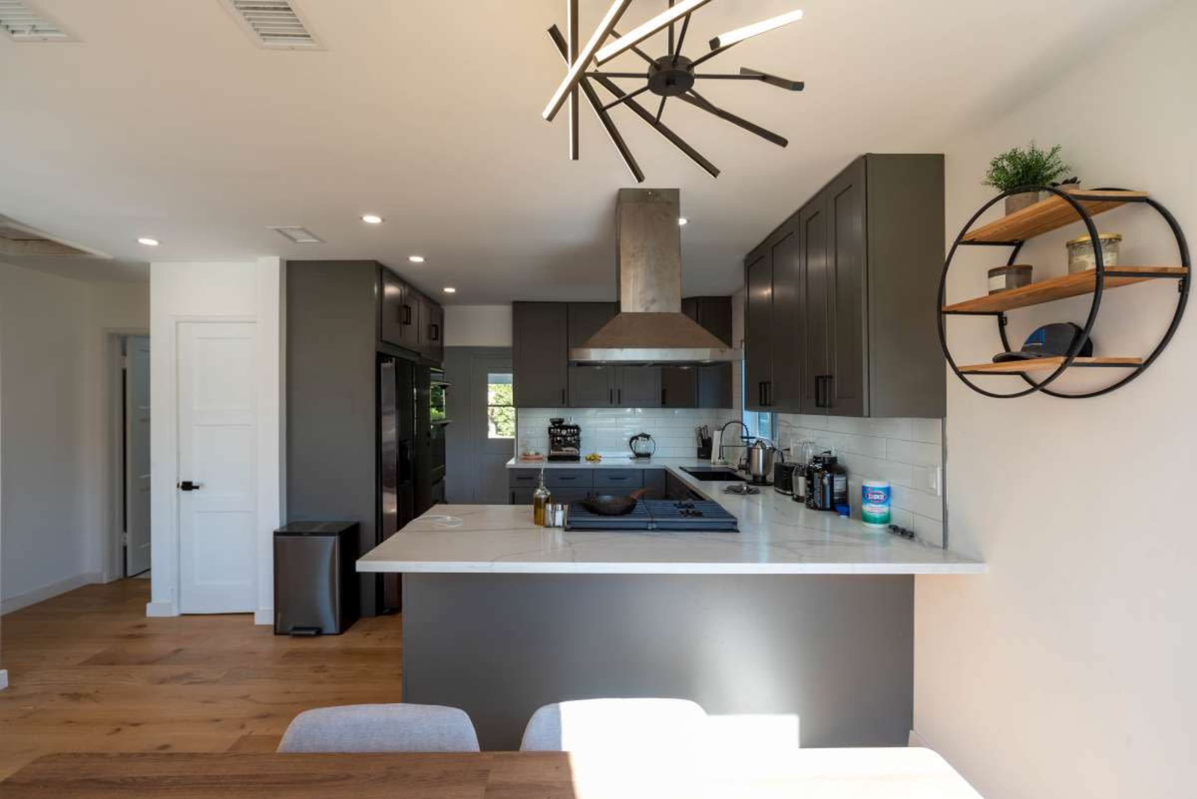 A modern kitchen featuring dark cabinetry, a central island with a stovetop, and a circular shelf mounted on the wall.