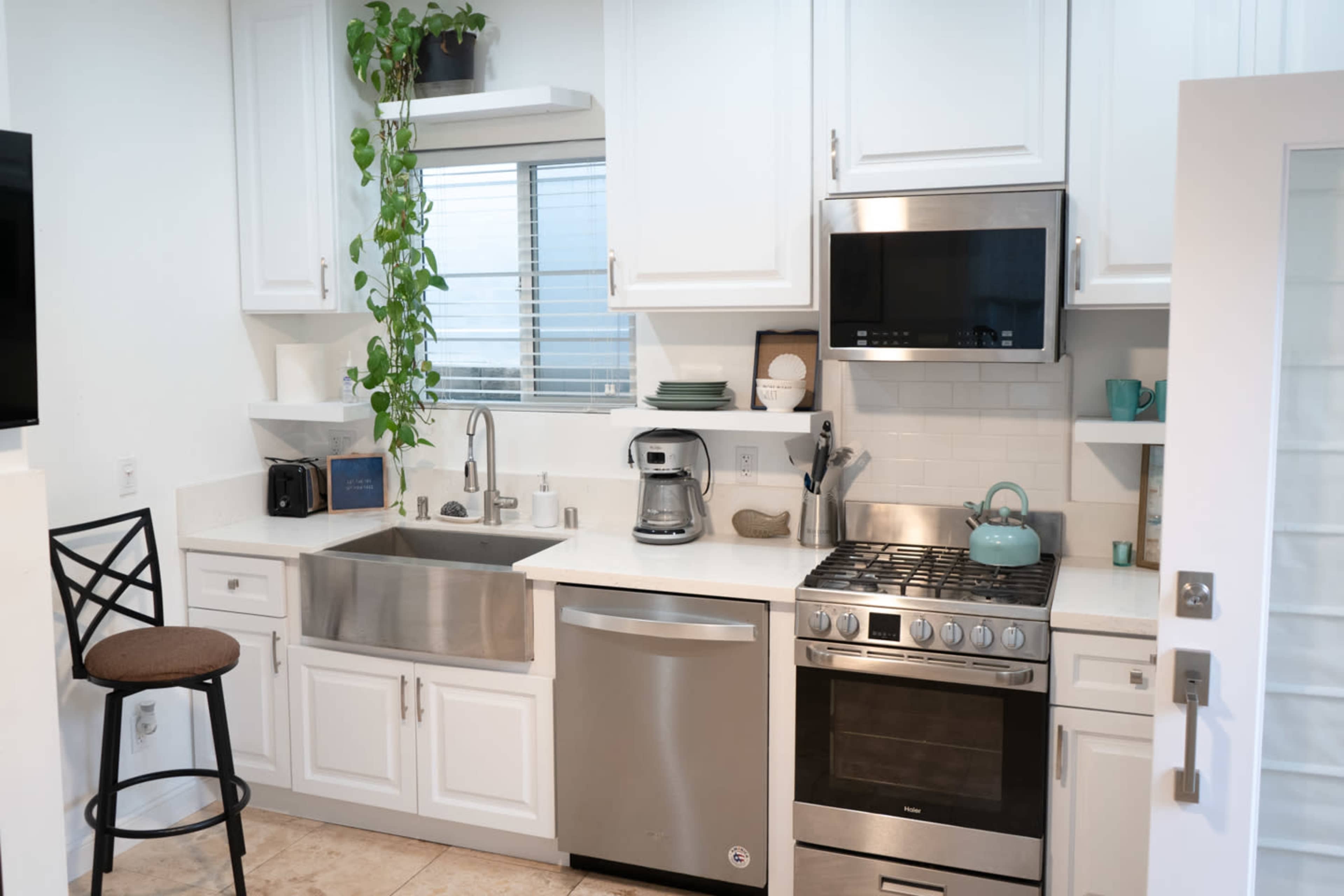 The image shows a modern kitchen featuring stainless steel appliances, white cabinetry, and a sink with a view to a small window.