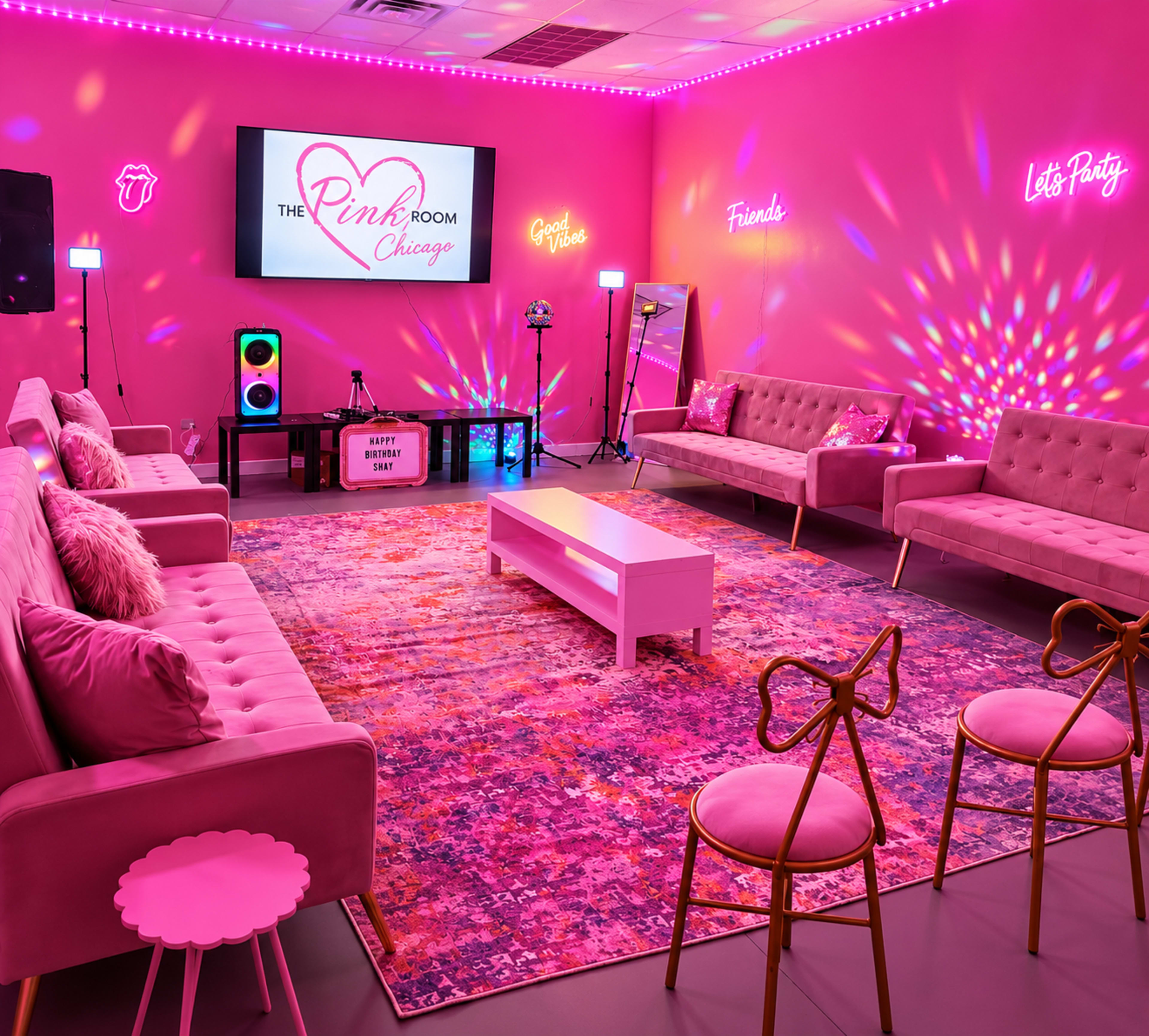 The image shows a vibrant room decorated in pink tones, featuring two plush sofas, a coffee table, a large screen displaying "The Pink Room Chicago," and colorful lighting effects.
