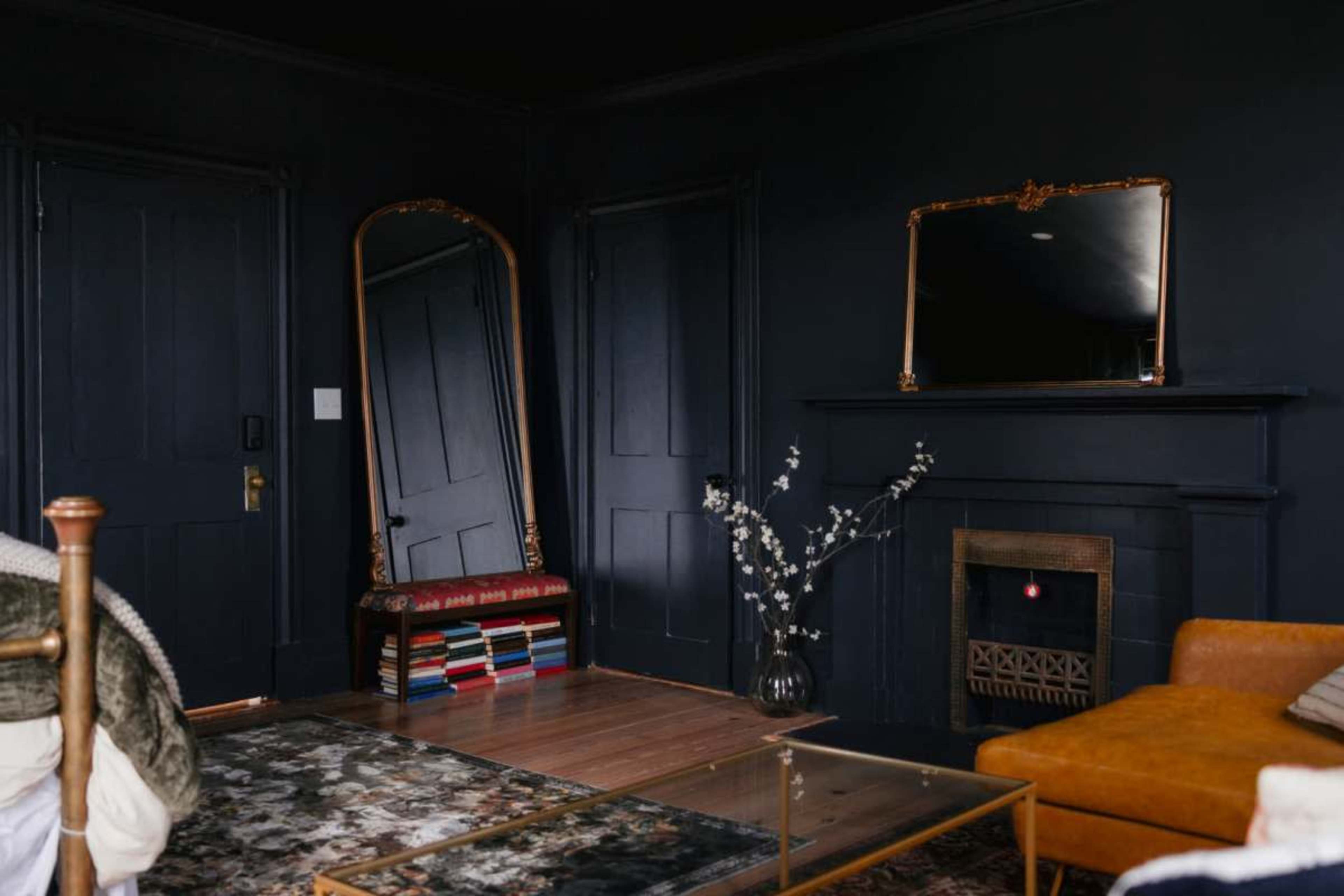 The image shows a darkly painted room with a large mirror, a fireplace, an orange sofa, and a decorative rug.