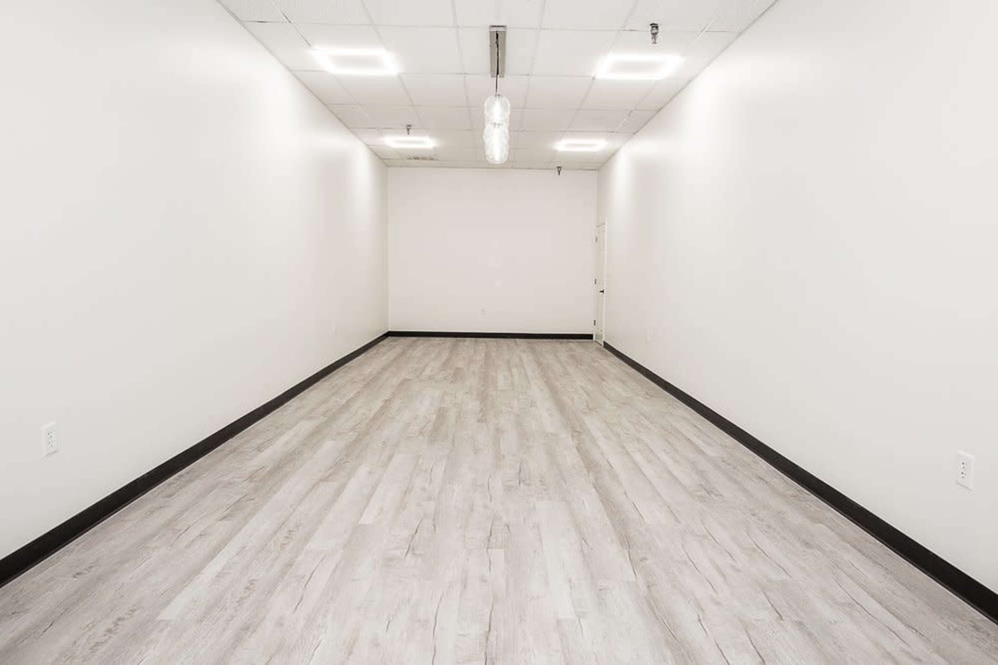 An empty, well-lit room with light-colored wooden flooring and white walls.