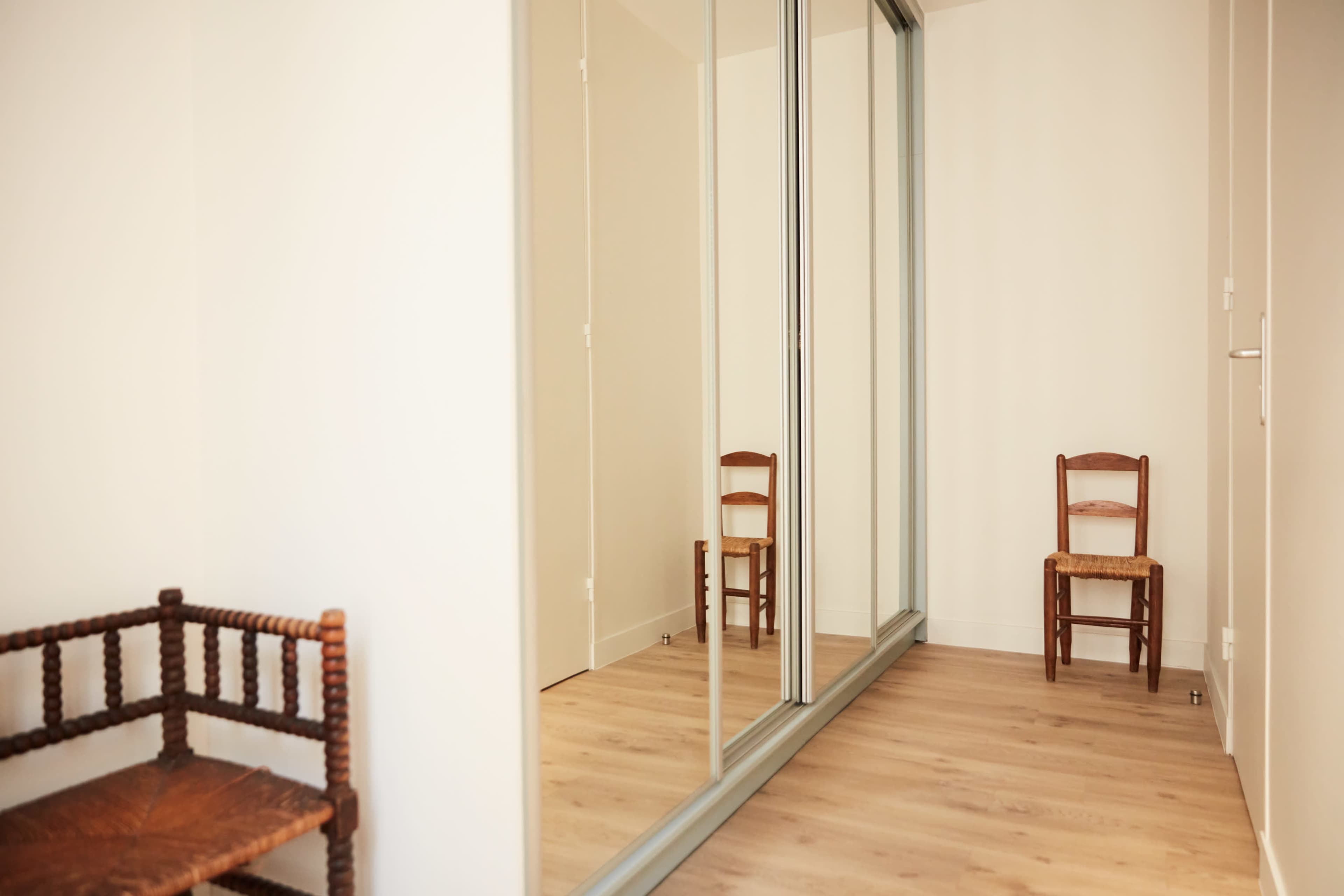 The scene shows a bright room with mirrored closet doors and two wooden chairs positioned on opposite sides.