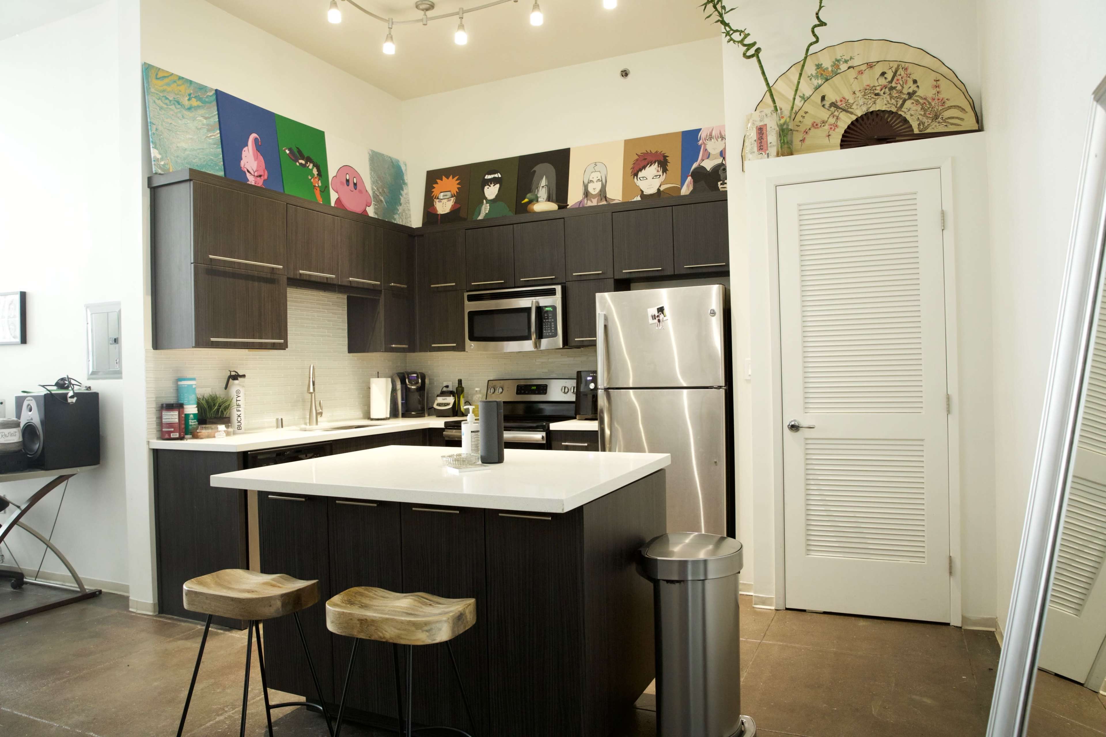 A modern kitchen with dark cabinetry, stainless steel appliances, a white island, and colorful artwork displayed on the wall above the cabinets.