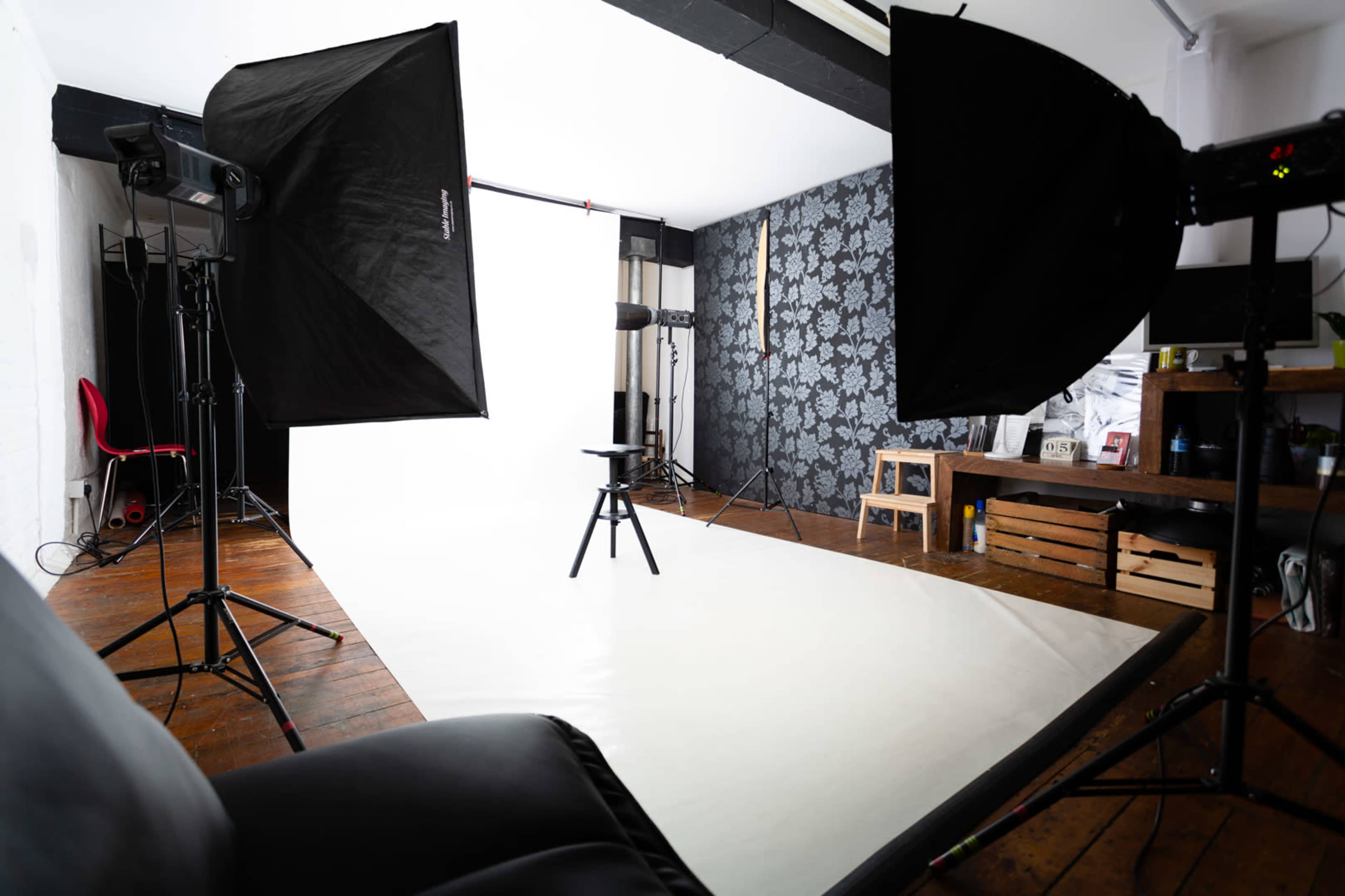 A photography studio setup with softbox lights, a backdrop, a stool in the center, and a dark-patterned wall in the background.