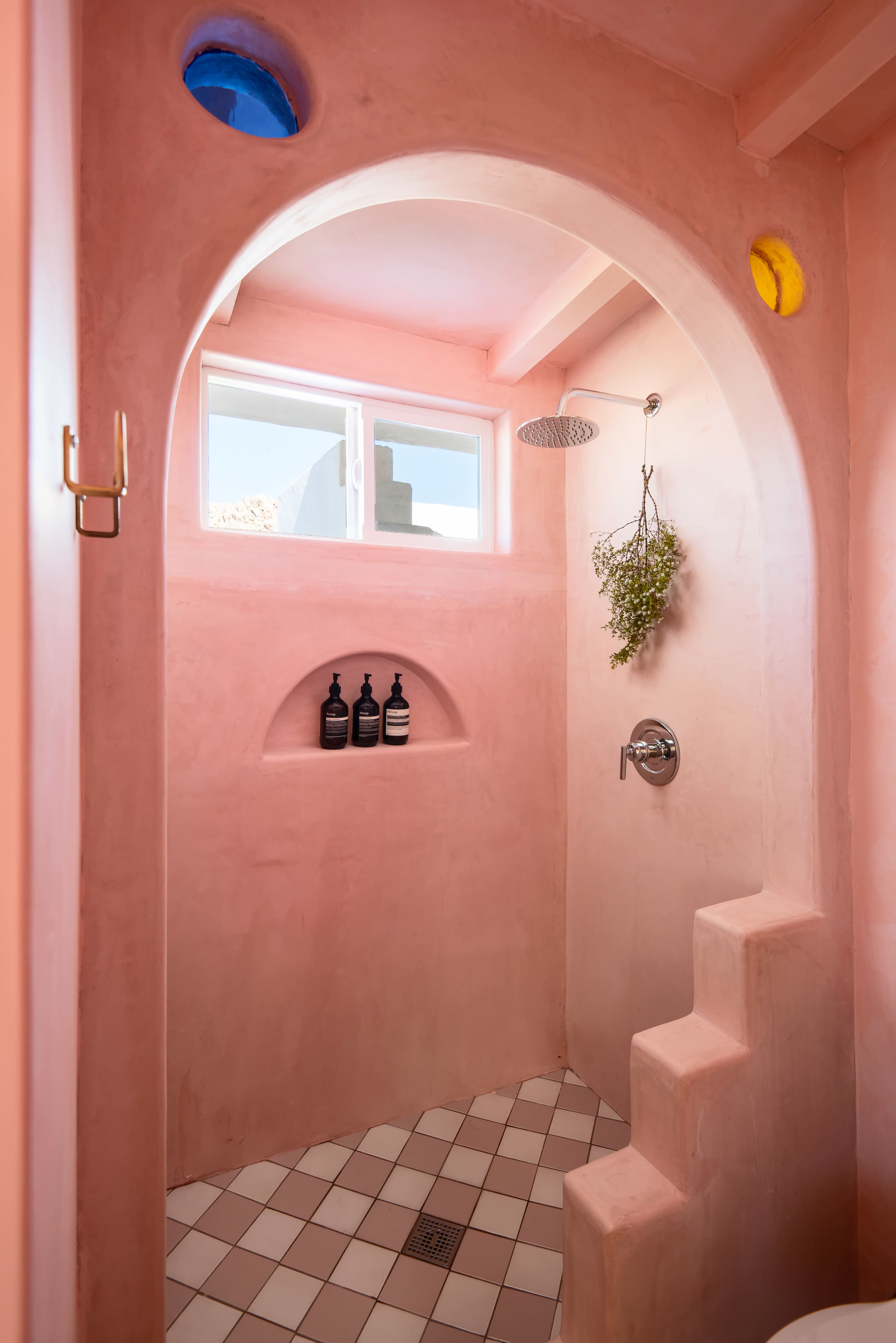 The image shows a pink plastered shower with a small staircase, an archway, and a window letting in natural light.
