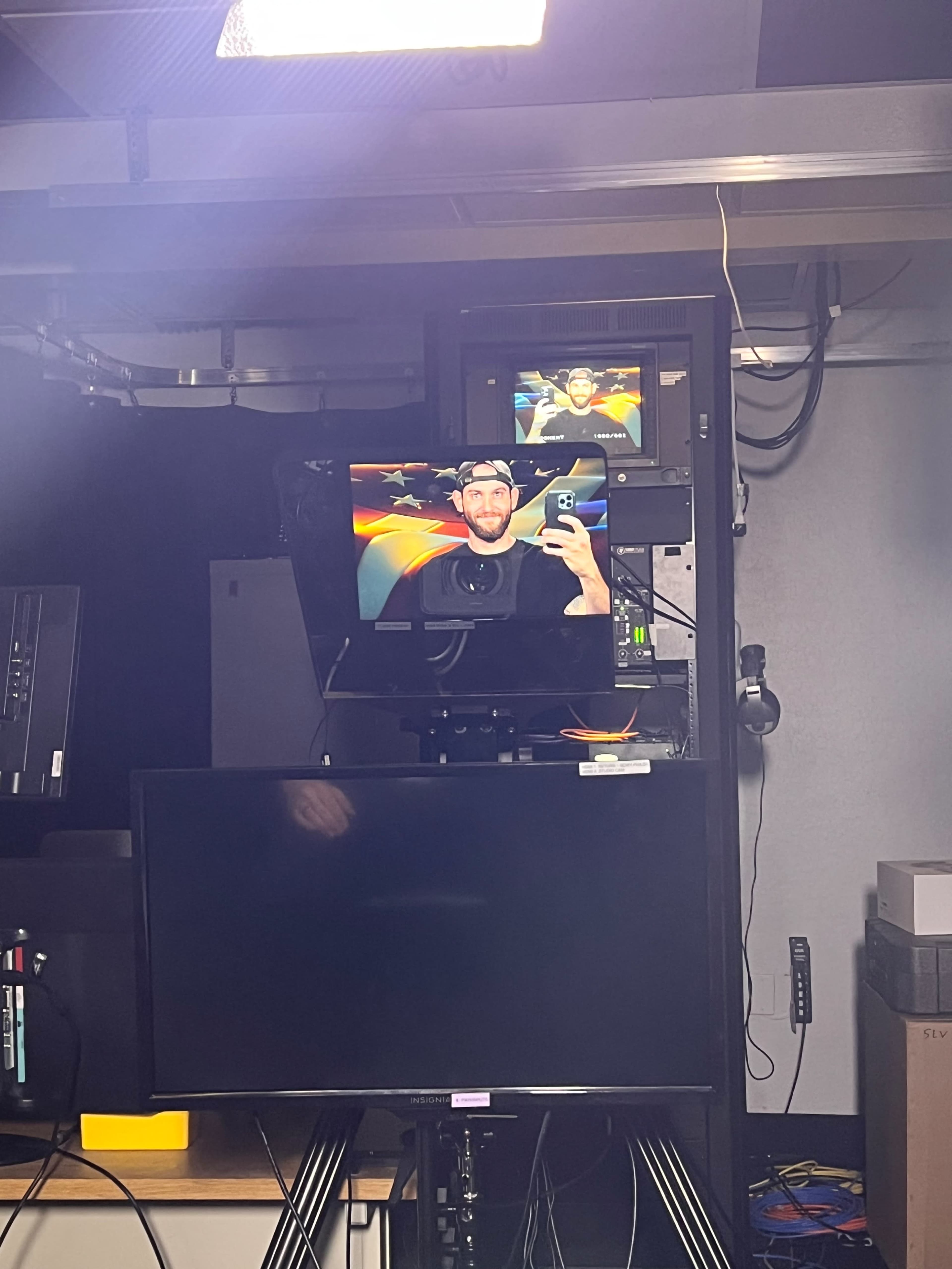 A man is posing for a selfie while surrounded by multiple screens in a studio-like environment.