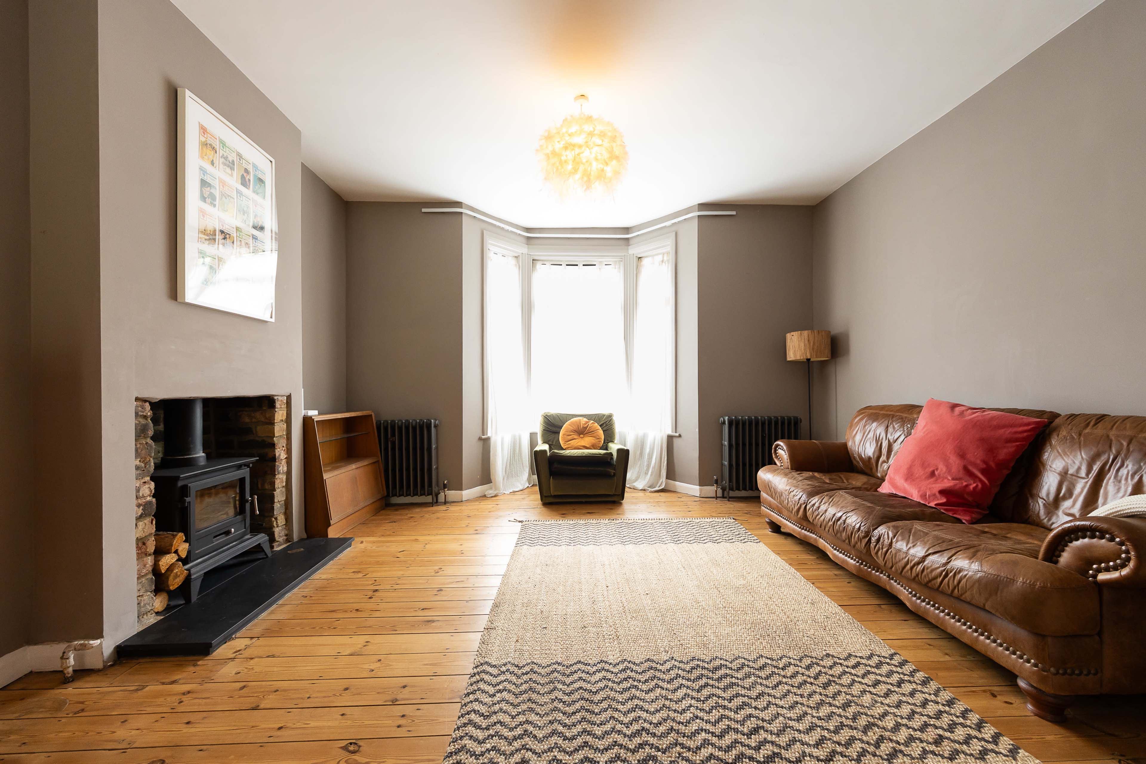 A spacious living room features a leather sofa, a wooden floor, and a fireplace, with large windows allowing natural light to enter.