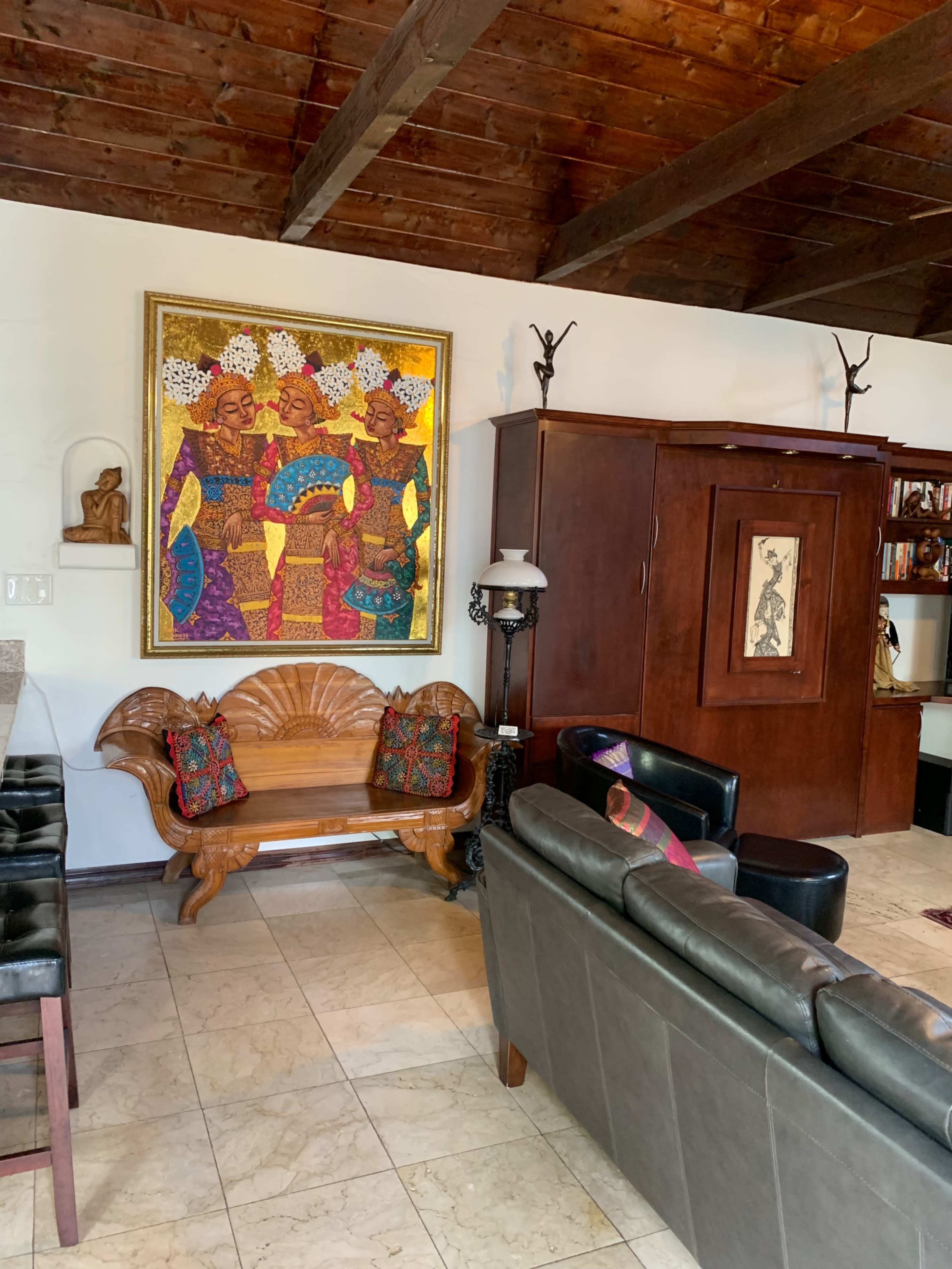 A living room with wooden beams, a large colorful art piece on the wall, a decorative wooden bench, and a dark leather sofa.