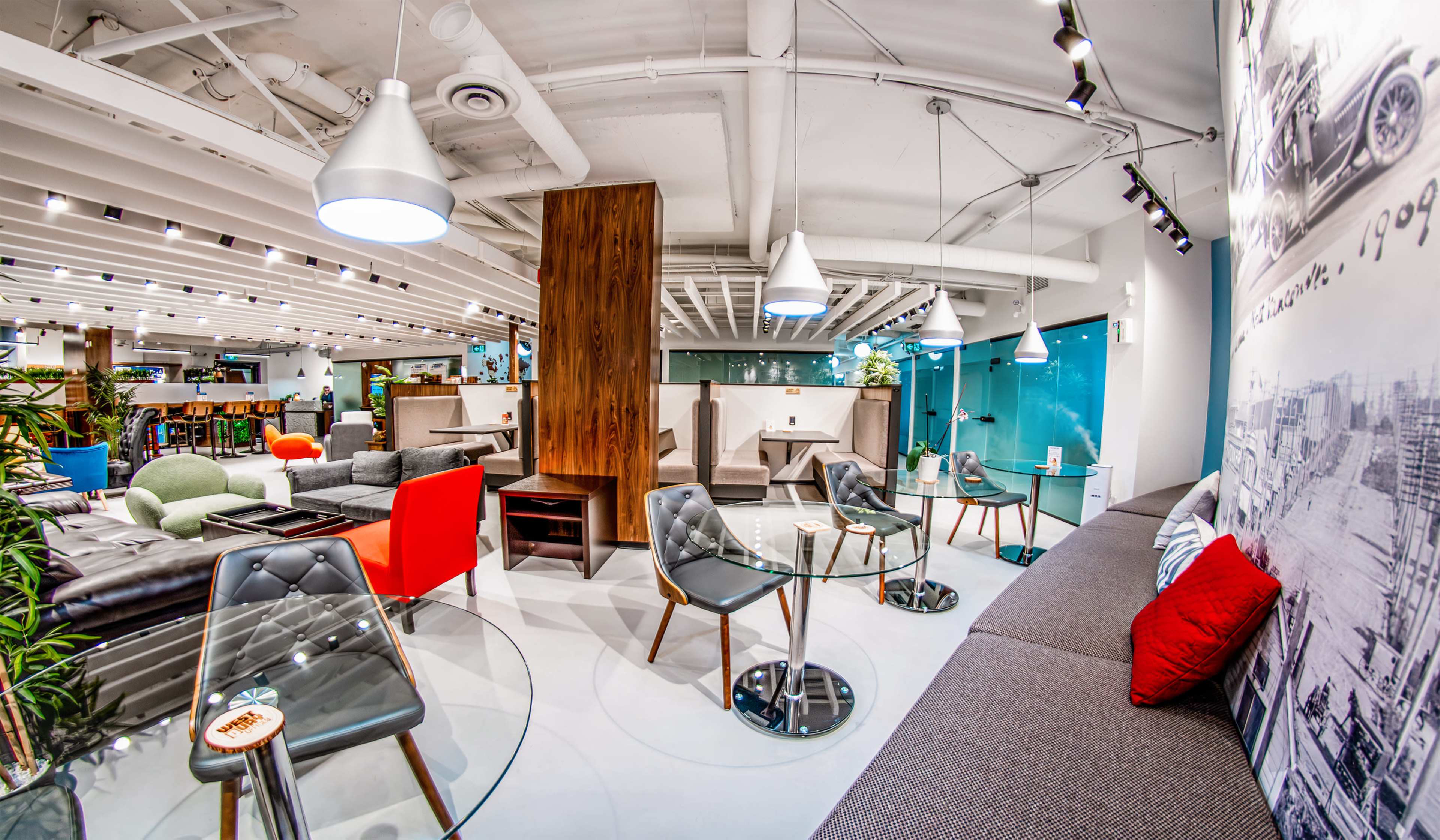 The image shows a modern, open seating area with various furniture arrangements, including glass tables and contemporary chairs, in a well-lit space.