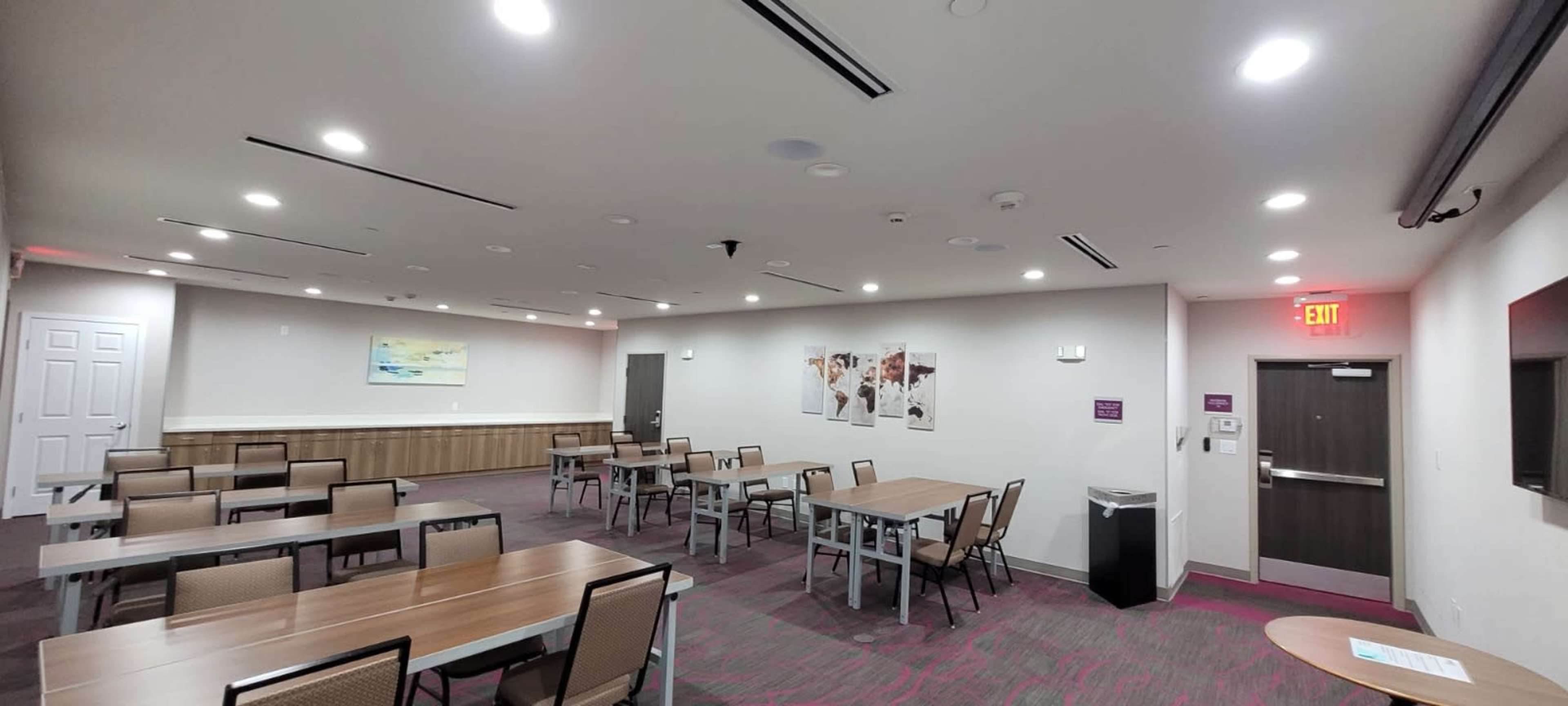 The image shows a modern meeting room with several tables and chairs arranged, light-colored walls, and artwork hanging on the wall.