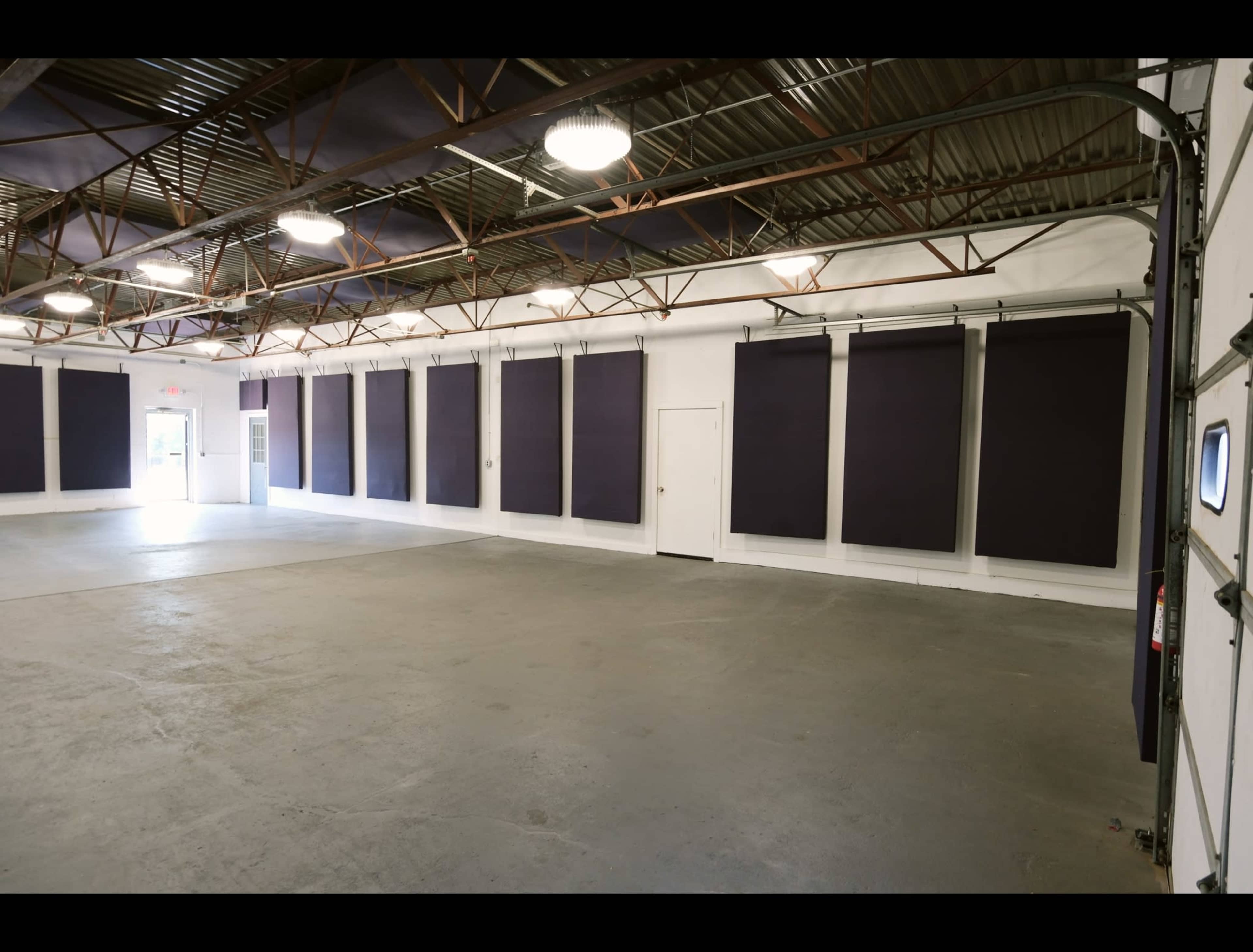 The image shows a spacious, empty room with concrete flooring and several large dark panels mounted on the walls.