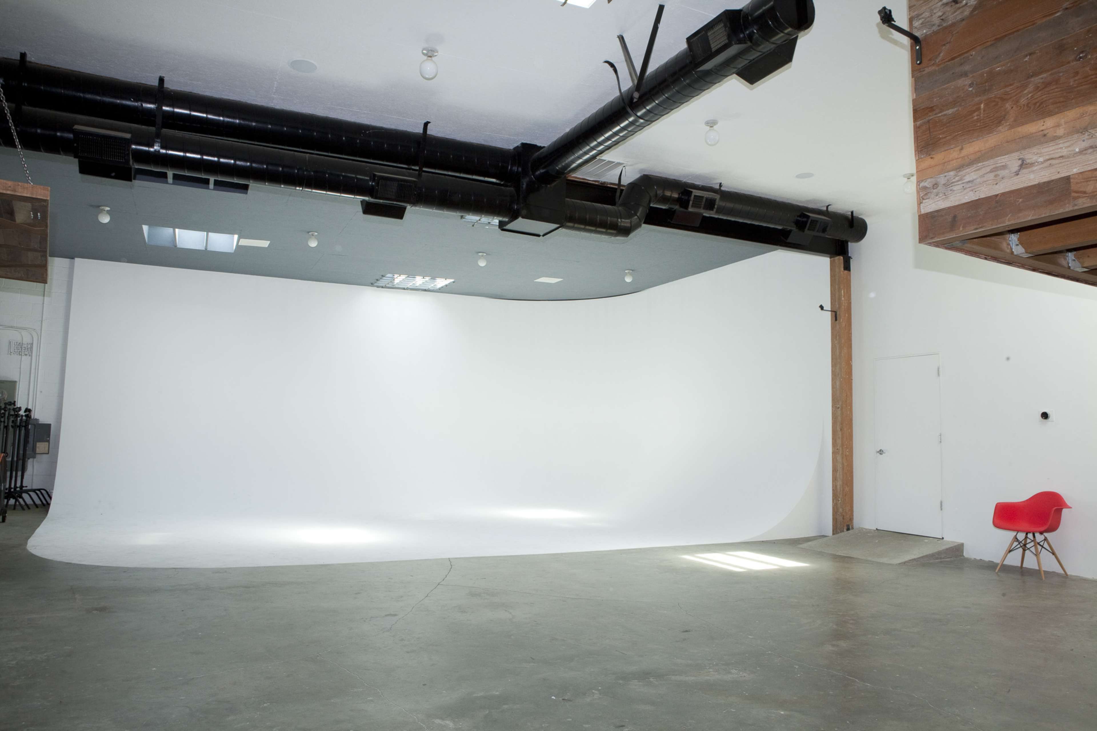 A spacious, empty studio with a white backdrop and industrial-style features, including exposed pipes and wooden elements.