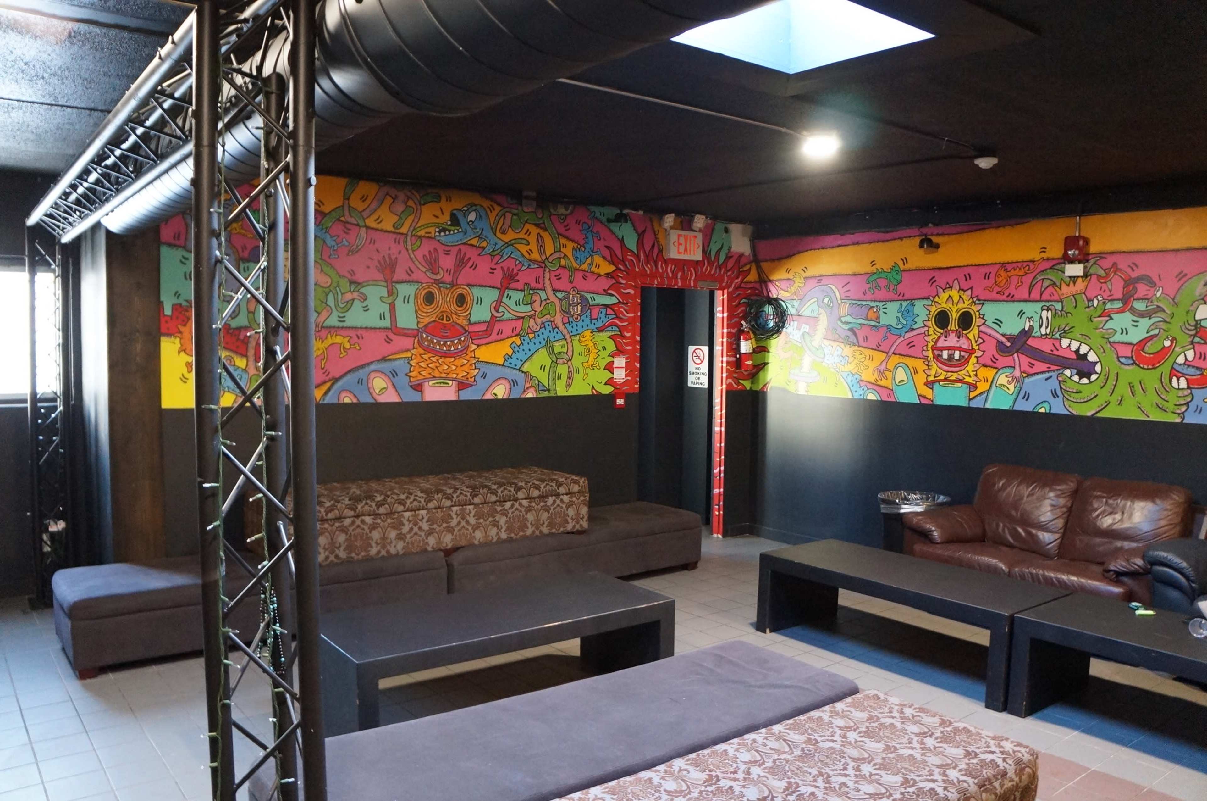 A lounge area with colorful mural-covered walls, several dark couches, and low tables under a black ceiling.