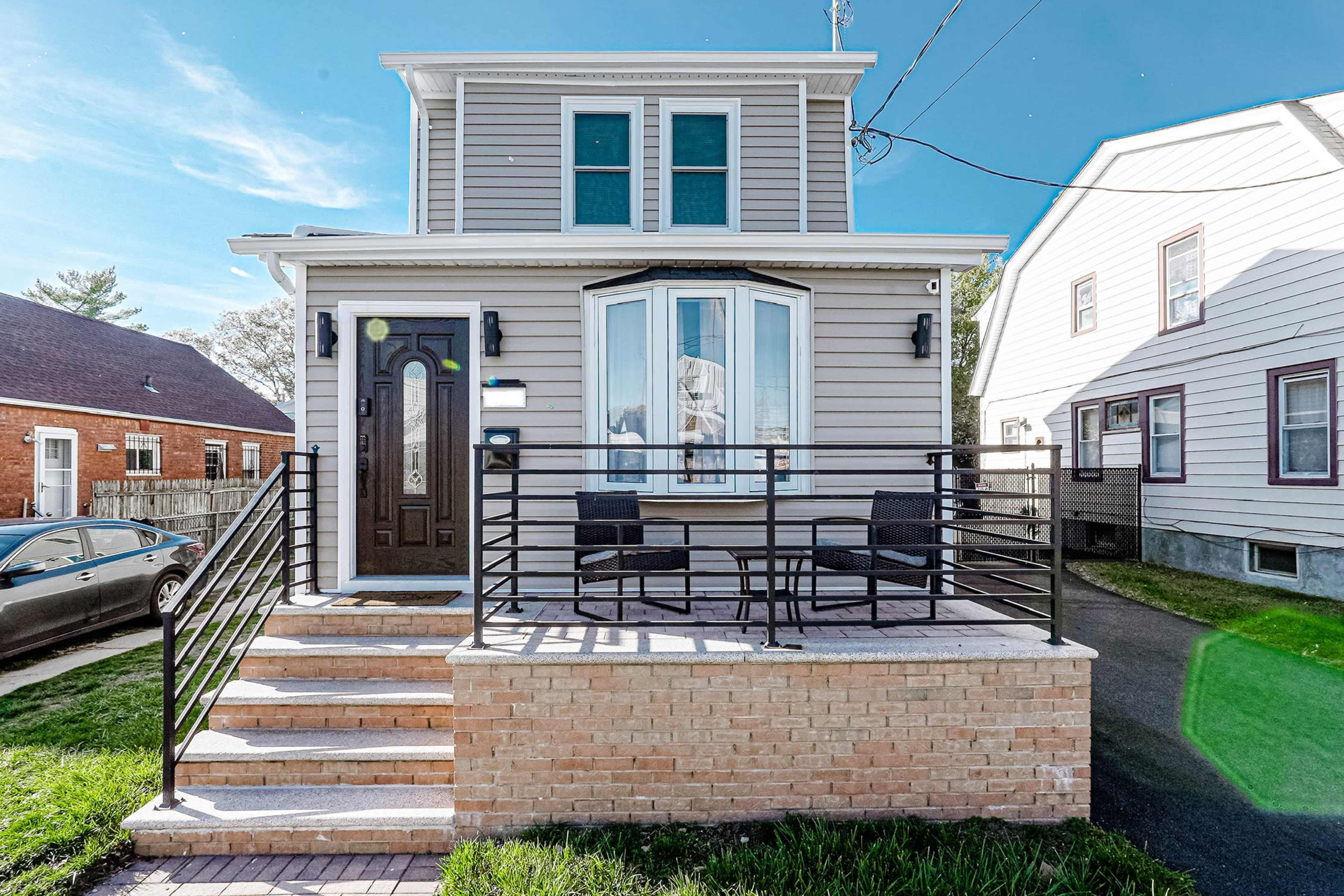 A two-story house with a front porch, featuring a set of chairs and steps leading to the entrance.